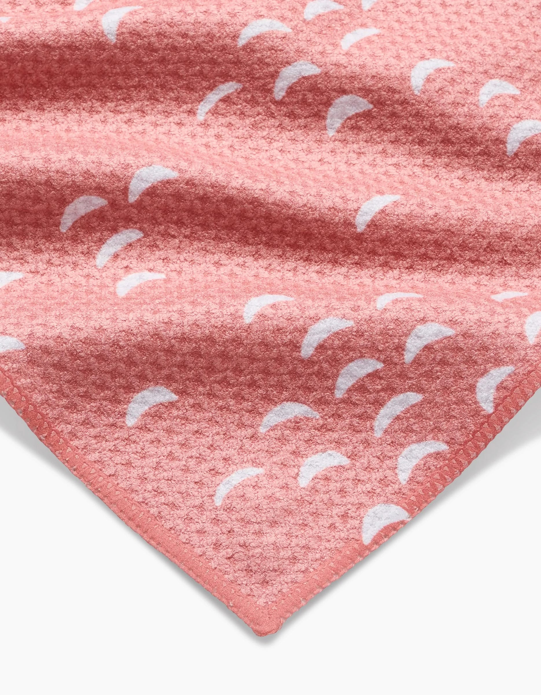 A close-up of the Windswept towel by Jessica Swift: a textured pink waffle weave made from recycled materials, featuring white crescent shapes and a neatly finished edge visible in the lower corner.