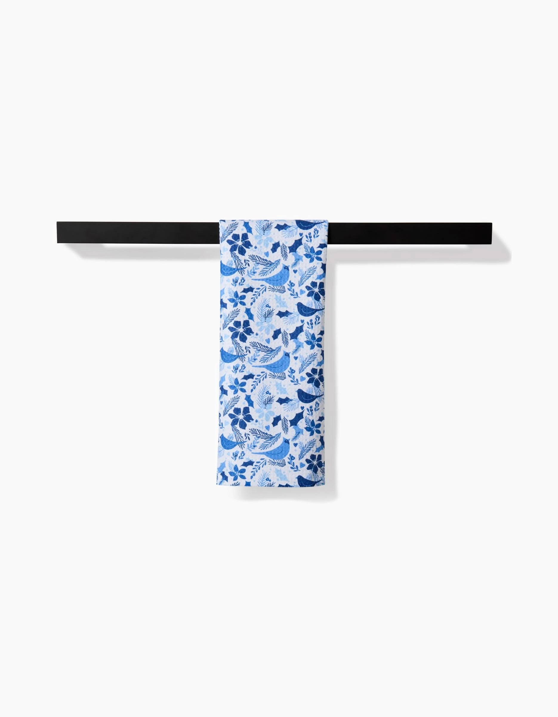 The Kris Ruff Winter Blue Birds towel, featuring a blue and white floral design, is neatly draped over a minimalist black horizontal rack against a plain white background.