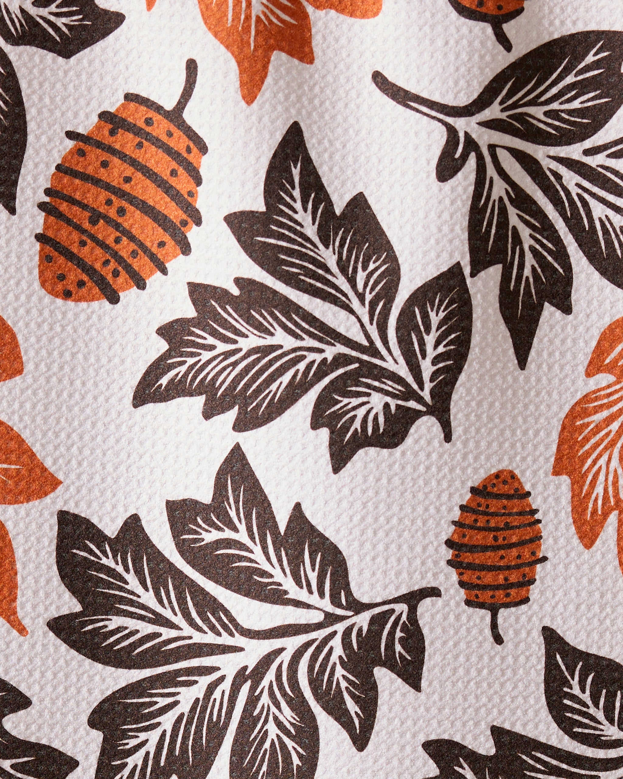 The Geometry Woodland Waltz bar towel features black leaves and orange pine cones on a white background with a textured, ultra-absorbent surface made from recycled materials.