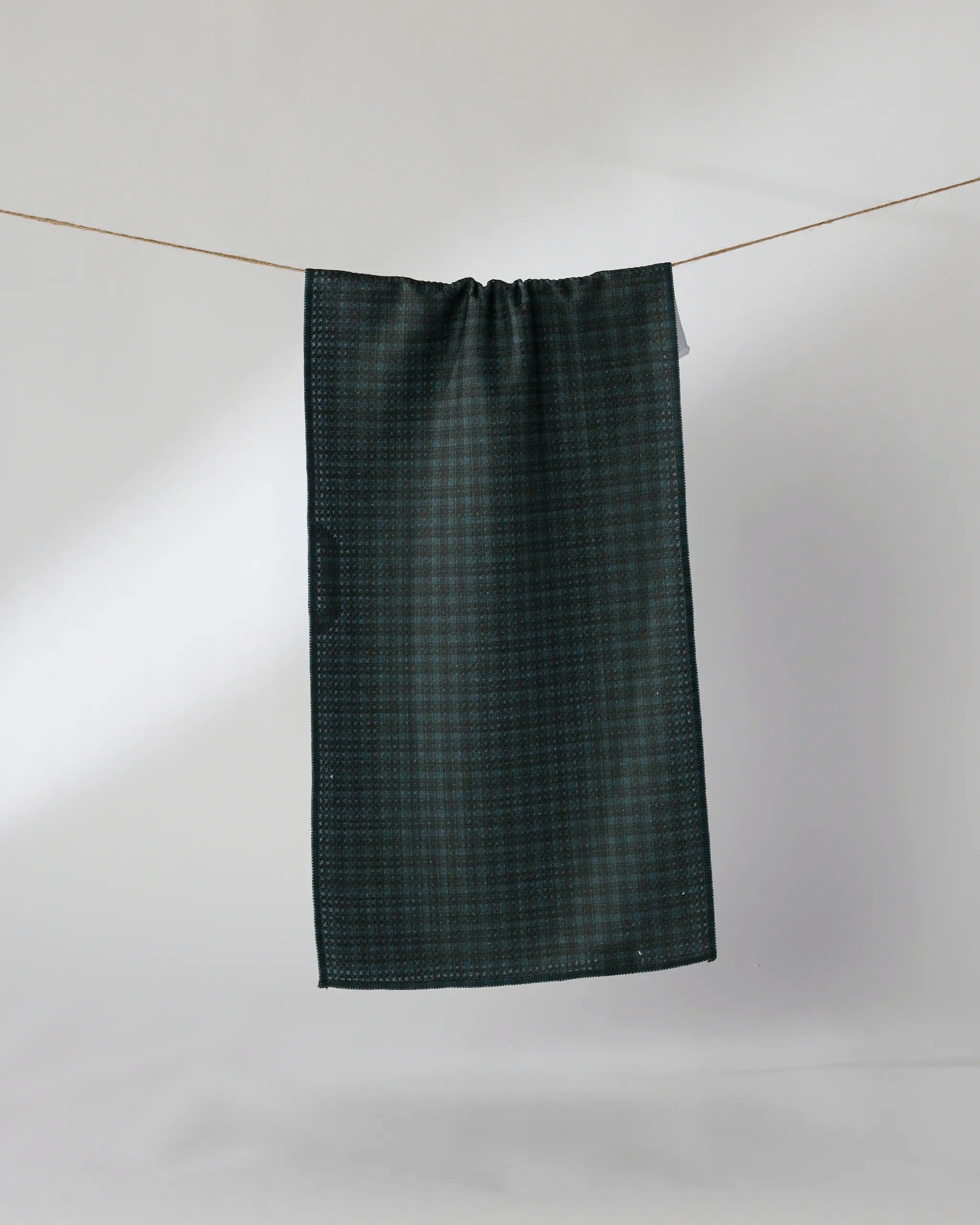 The Geometry Wren towel, featuring a dark green textured design and quick-drying fabric, hangs neatly on a clothesline against a plain light gray background.