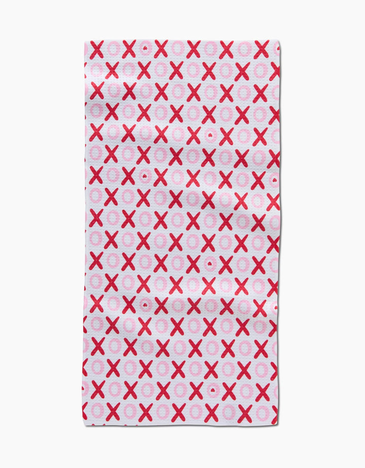 The XOXO bar towel by Sarah Daugherty is a rectangular white towel made from recycled materials, featuring a grid of repeating red and pink Xs and Os.