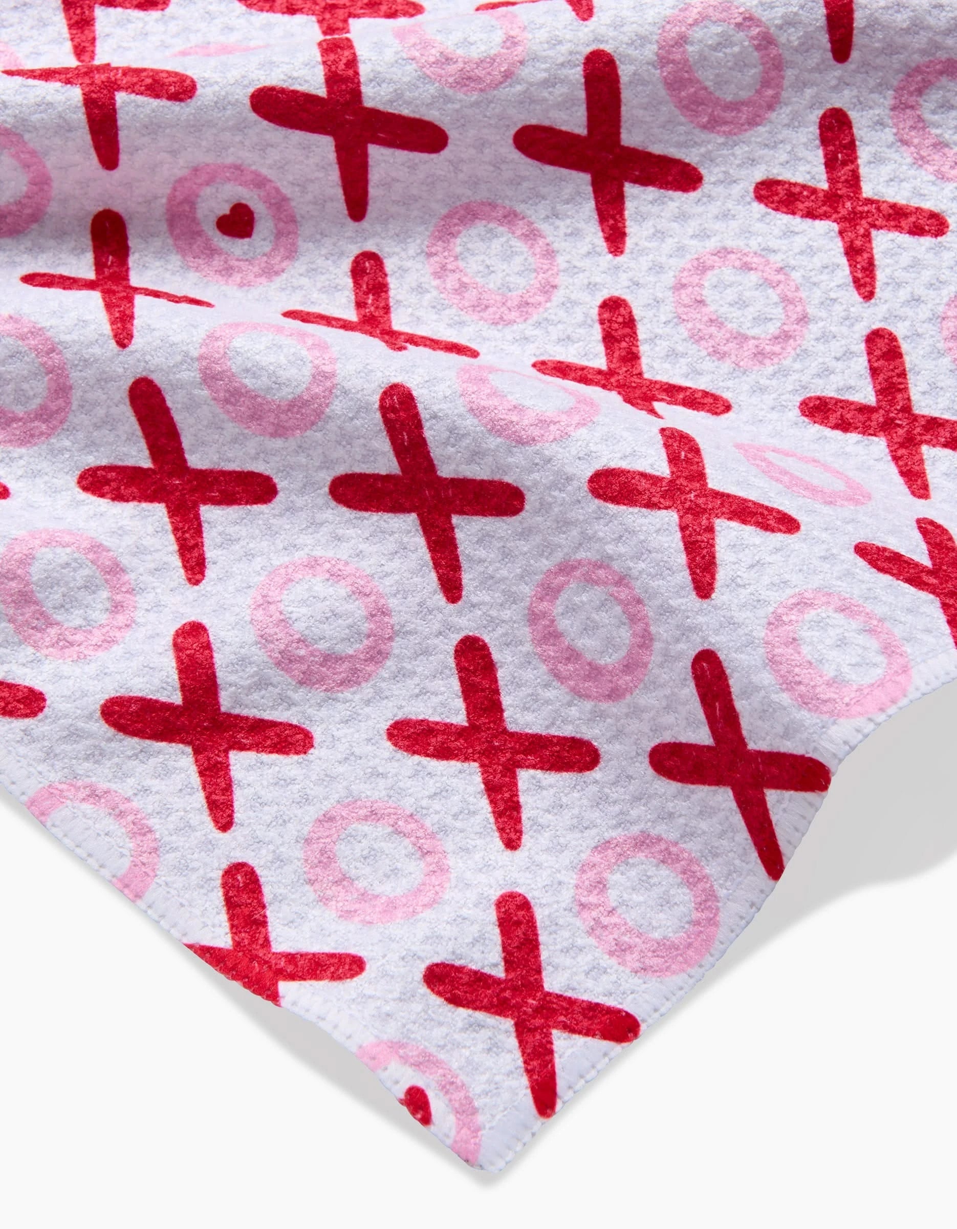 The XOXO towel by Sarah Daugherty is ultra-absorbent and soft, featuring a white base with red Xs and pink Os in a hugs and kisses pattern, shown slightly folded to highlight its texture.