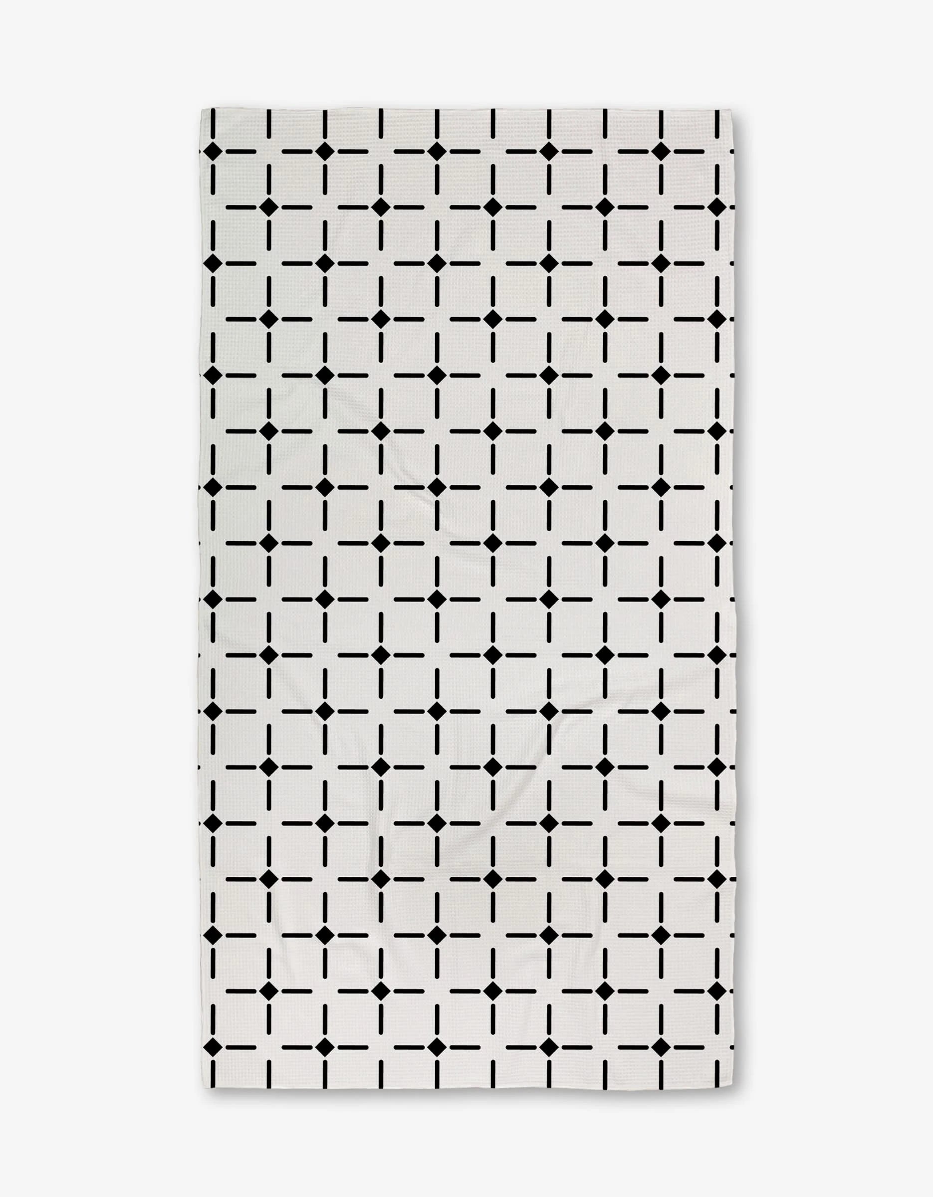 The Collins Luxe Bath Towel by Charlie Rowan Designs is a white rectangular towel featuring a repeating geometric grid of black squares and dots, crafted using innovative Geoweave technology for symmetry and style.