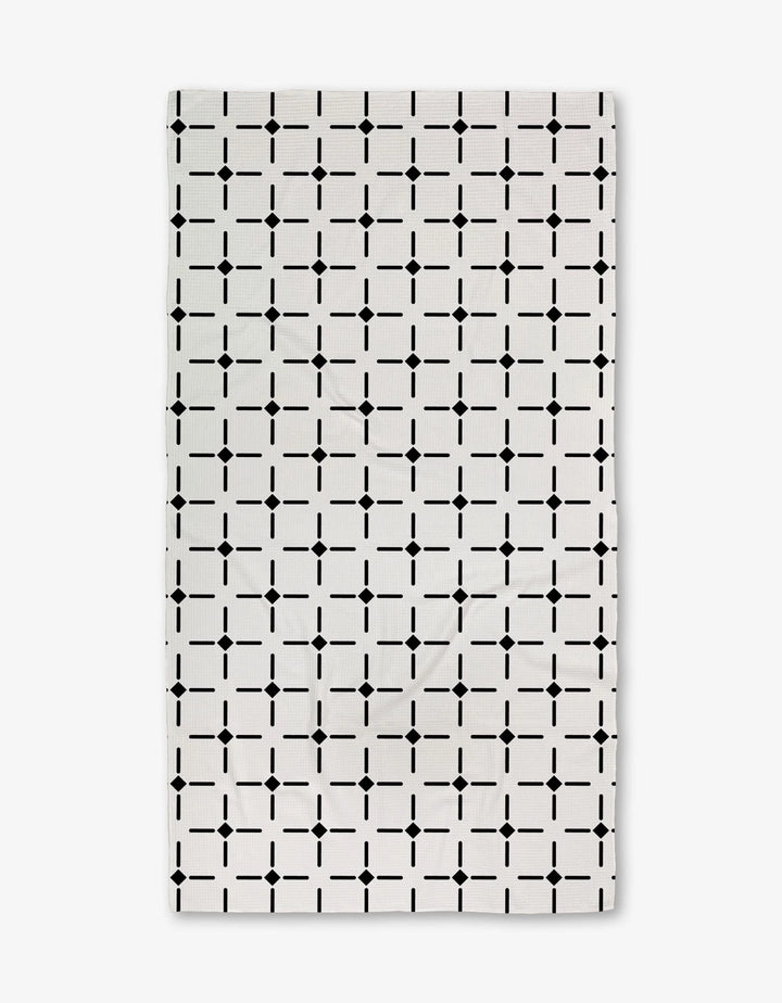 The Collins Luxe Bath Towel by Charlie Rowan Designs is a white rectangular towel featuring a repeating geometric grid of black squares and dots, crafted using innovative Geoweave technology for symmetry and style.
