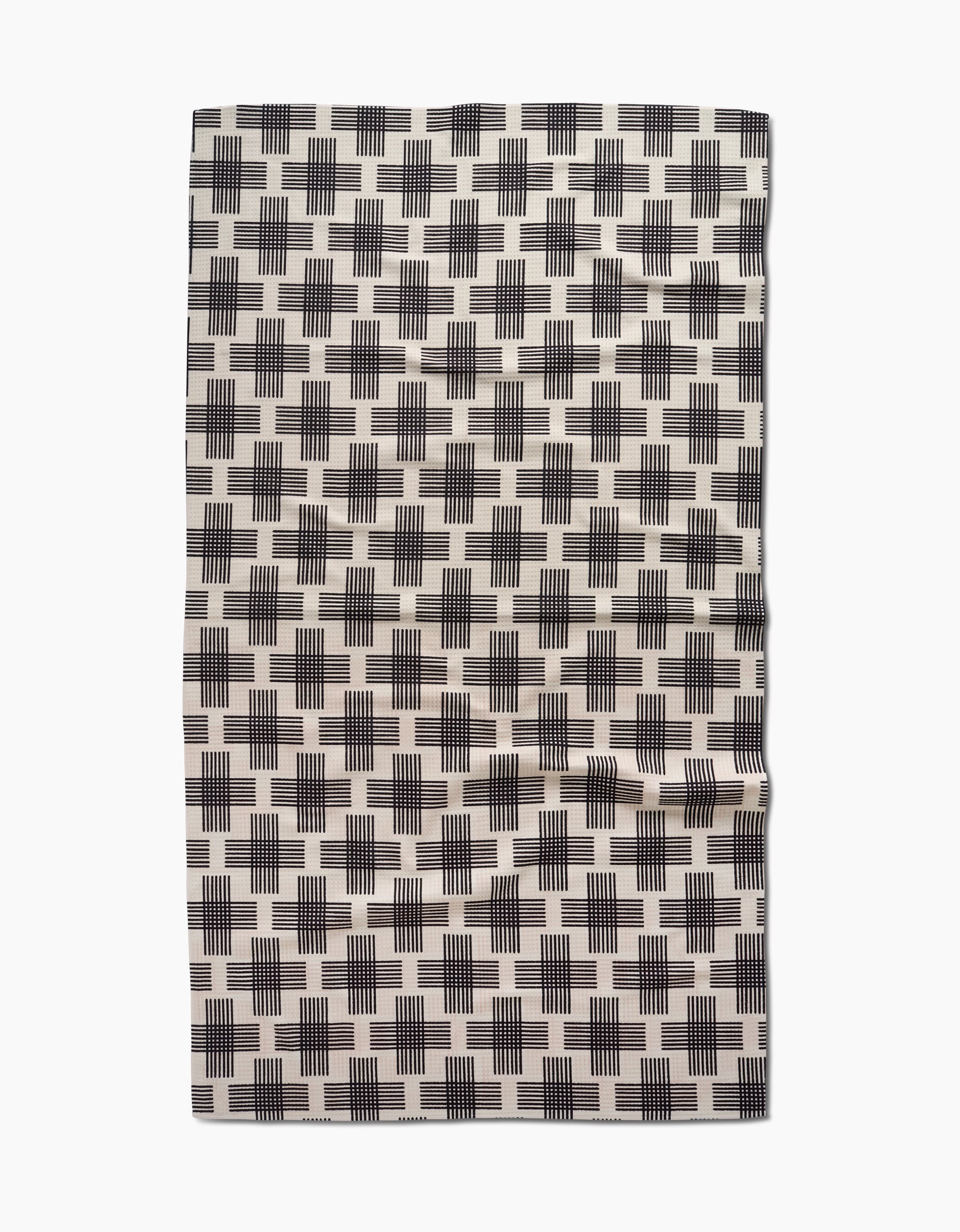 The Cross Hatch Luxe Bath Towel by Rosa Kichline features a cream base with black plus-sign patterns and a slightly wrinkled appearance, crafted using advanced Geoweave technology.