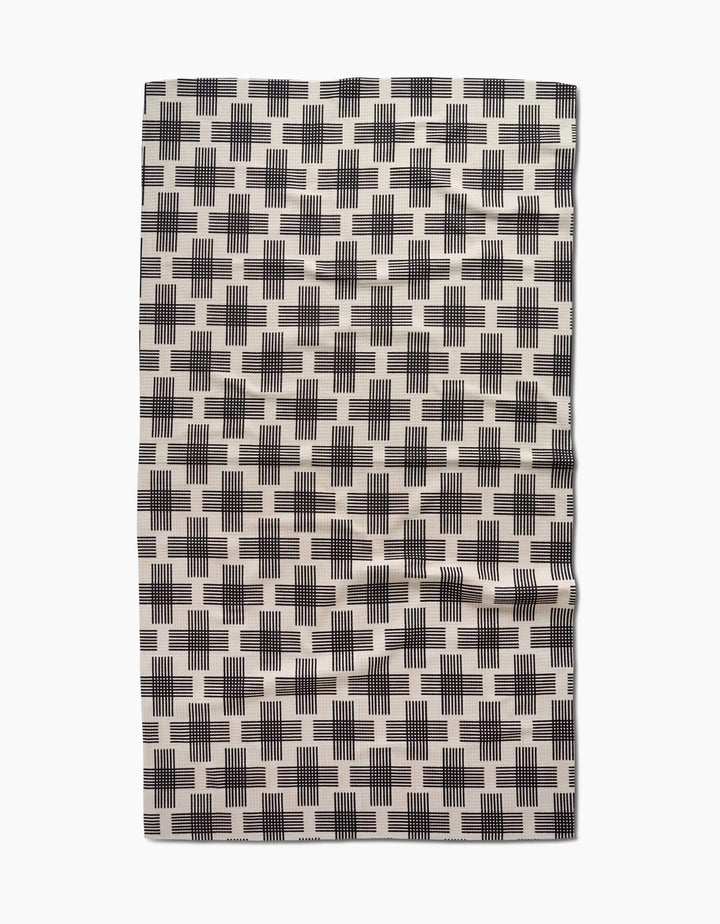 The Cross Hatch Luxe Bath Towel by Rosa Kichline features a cream base with black plus-sign patterns and a slightly wrinkled appearance, crafted using advanced Geoweave technology.