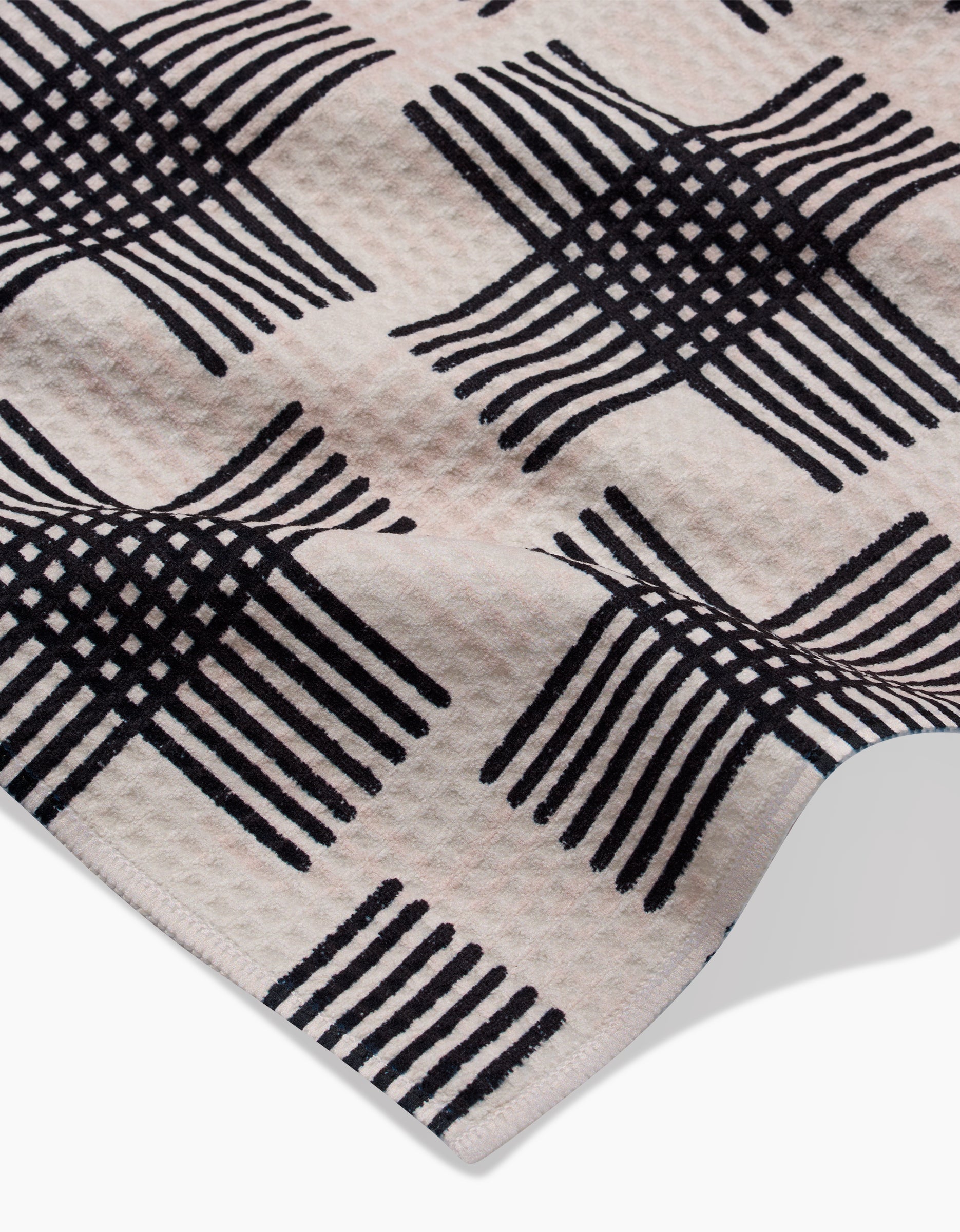 A close-up of Rosa Kichline’s Cross Hatch towel shows its ultra-absorbent Geoweave fabric and raised corner, featuring a repeating black geometric pattern of interlocking lines on a light background.