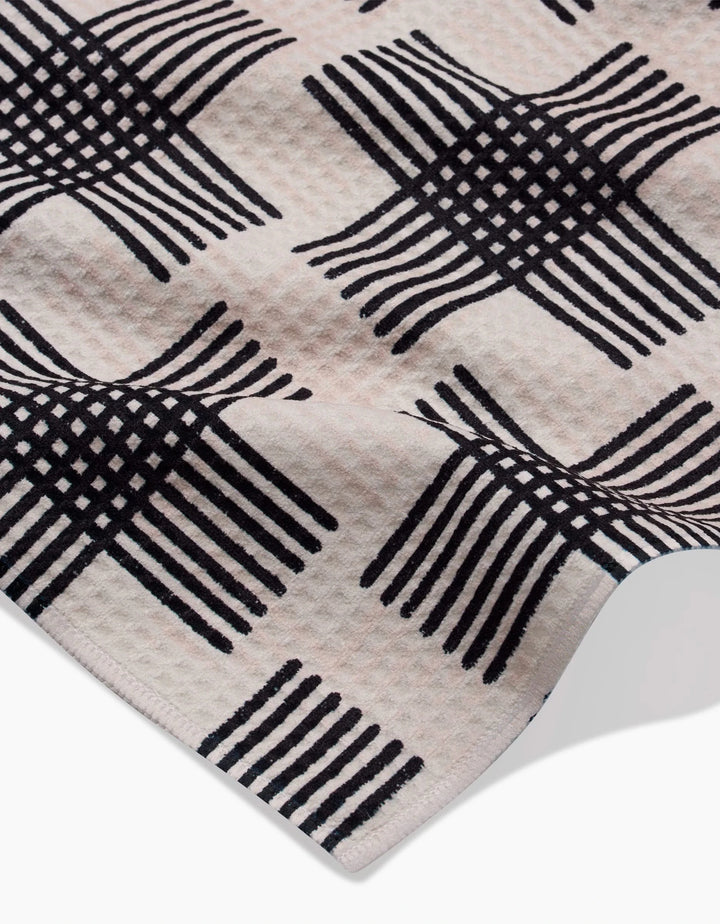 A close-up of Rosa Kichline’s Cross Hatch towel shows its ultra-absorbent Geoweave fabric and raised corner, featuring a repeating black geometric pattern of interlocking lines on a light background.