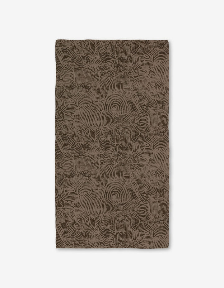 The Imprint rug by Studio Jeannot is a rectangular brown rug featuring an abstract, textured pattern of swirling lines on a white background, crafted with ultra-absorbent Geoweave technology for enhanced comfort.