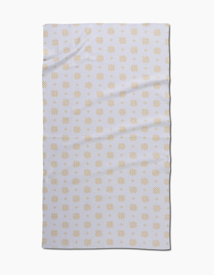 The Danelys Sidron Morning Petals bath towel is rectangular and white, featuring a repeating pattern of small yellow sunbursts. Slightly wrinkled, the towel is displayed on a plain white background.