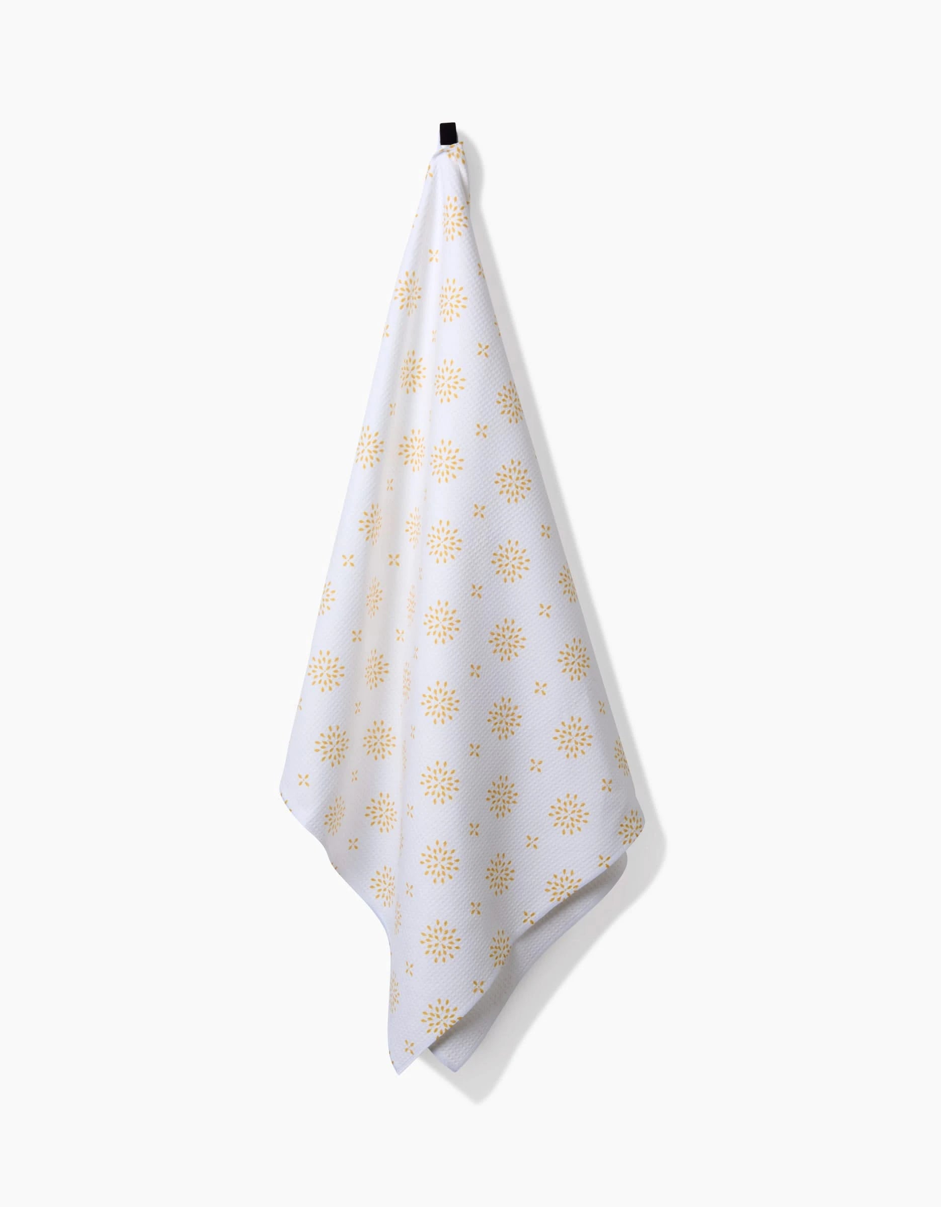 The Morning Petals Luxe Bath Towel by Danelys Sidron, featuring yellow sunburst shapes and crafted with Geoweave technology for superior absorbency and quick drying, hangs from a black hook against a plain white background.