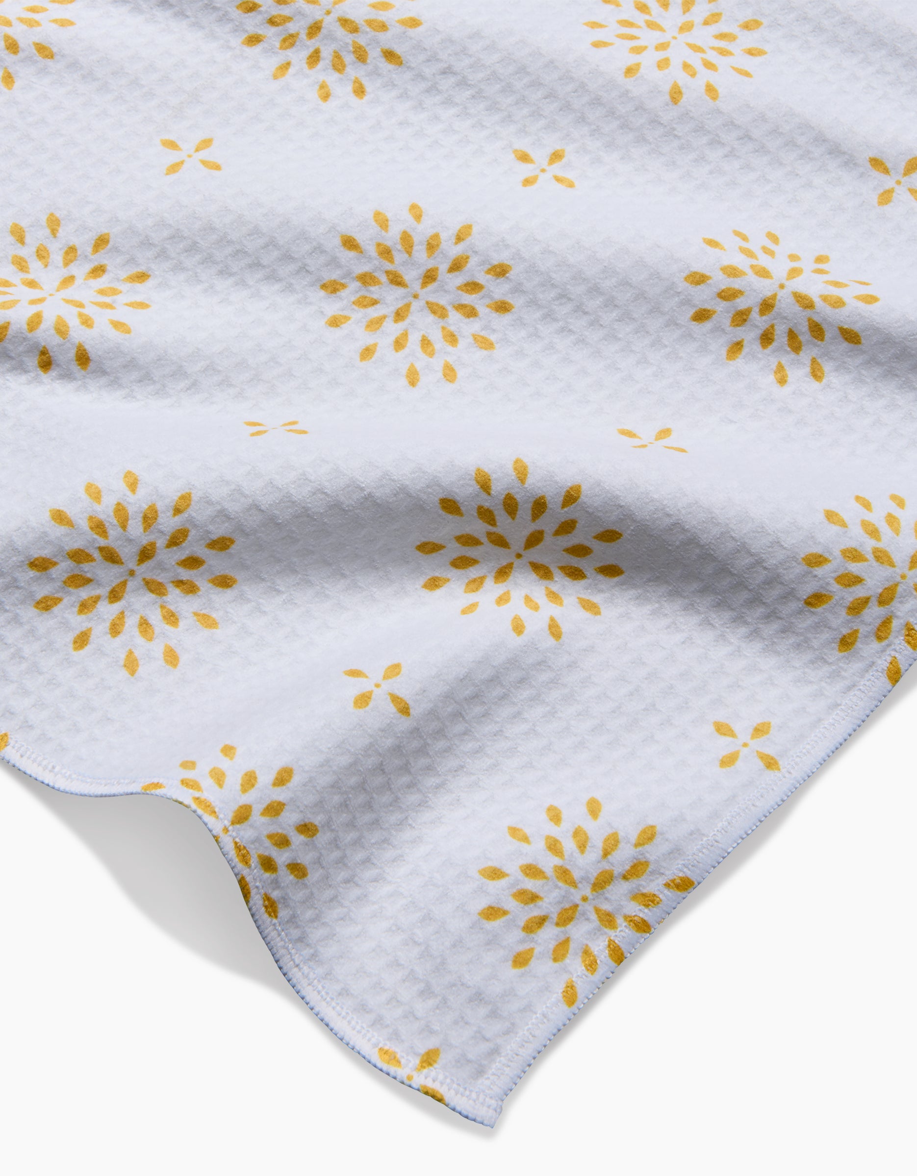 The Morning Petals bath towel by Danelys Sidron features a white textured waffle pattern with a repeating yellow floral burst design, shown slightly rumpled against a white background.
