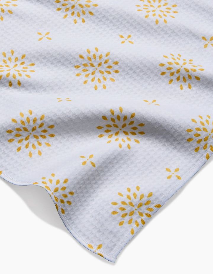 The Morning Petals bath towel by Danelys Sidron features a white textured waffle pattern with a repeating yellow floral burst design, shown slightly rumpled against a white background.