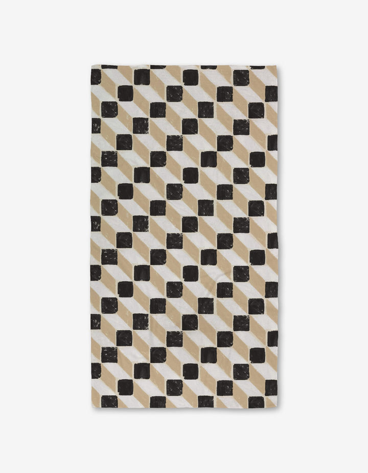 The Studio Jeannot Tessera Luxe Bath Towel features a geometric pattern of black squares and diagonal beige lines on white, crafted with Geoweave technology for ultra-absorbency.
