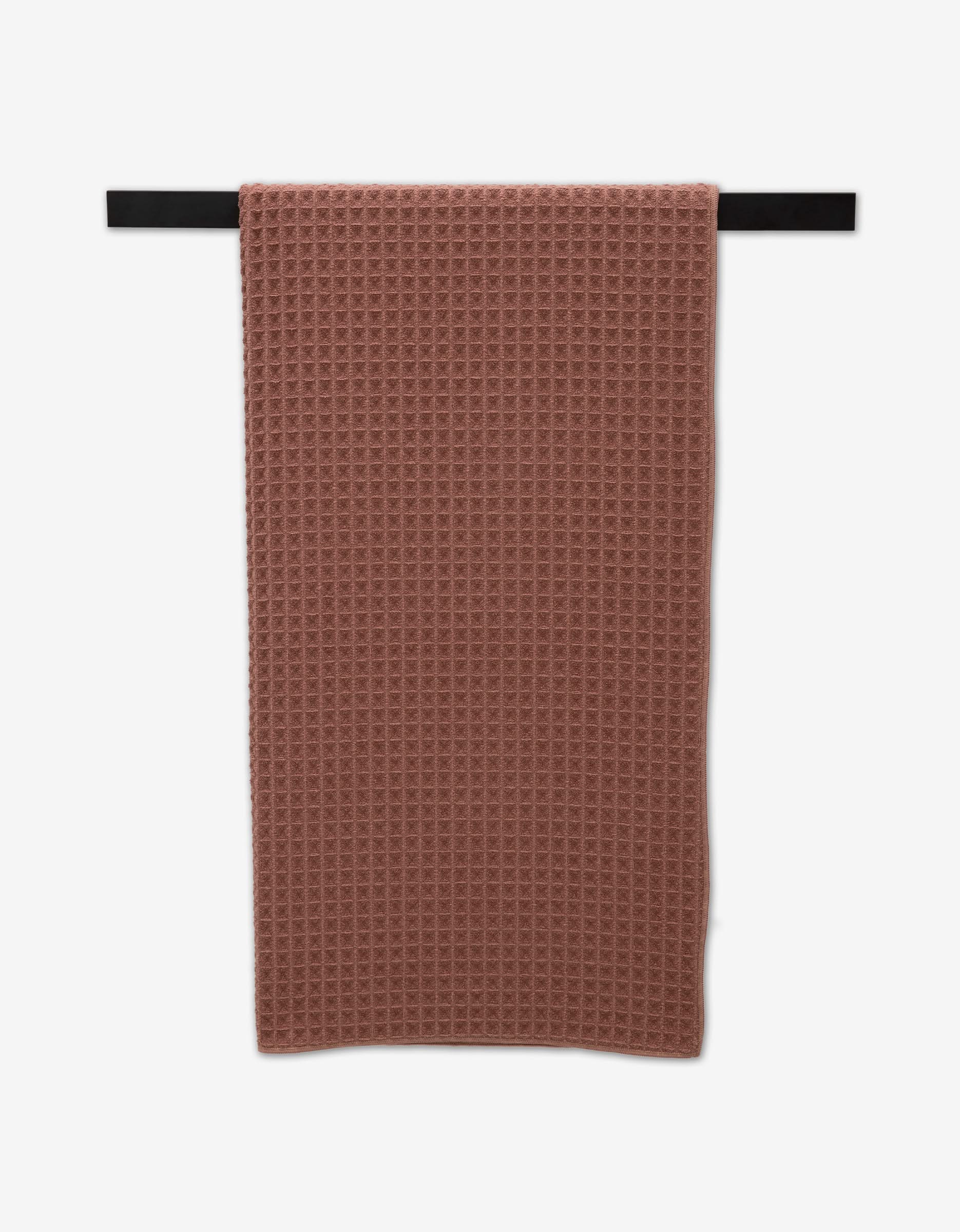 A GEOMETRY Waffle Bath Towel in Dusty Rose is neatly draped over a horizontal black towel bar against a white background.