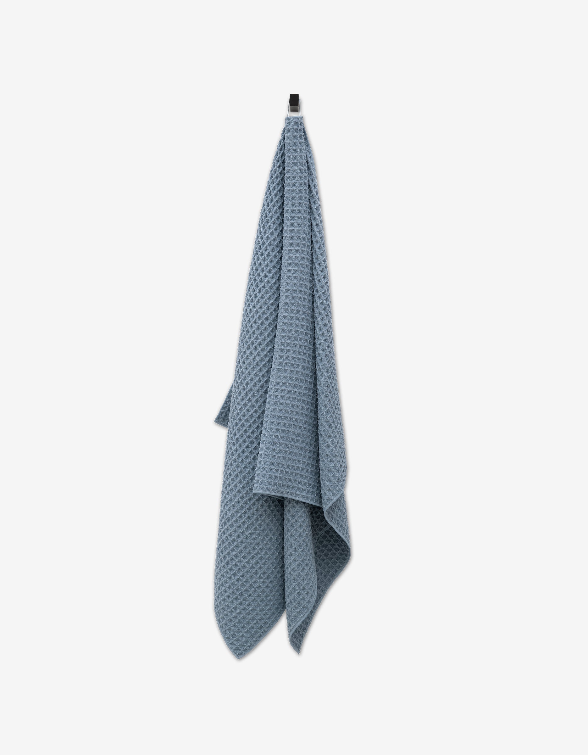 The GEOMETRY Sky Waffle Bath Towel, featuring an ultra-absorbent texture, hangs from a hook against a plain white background.