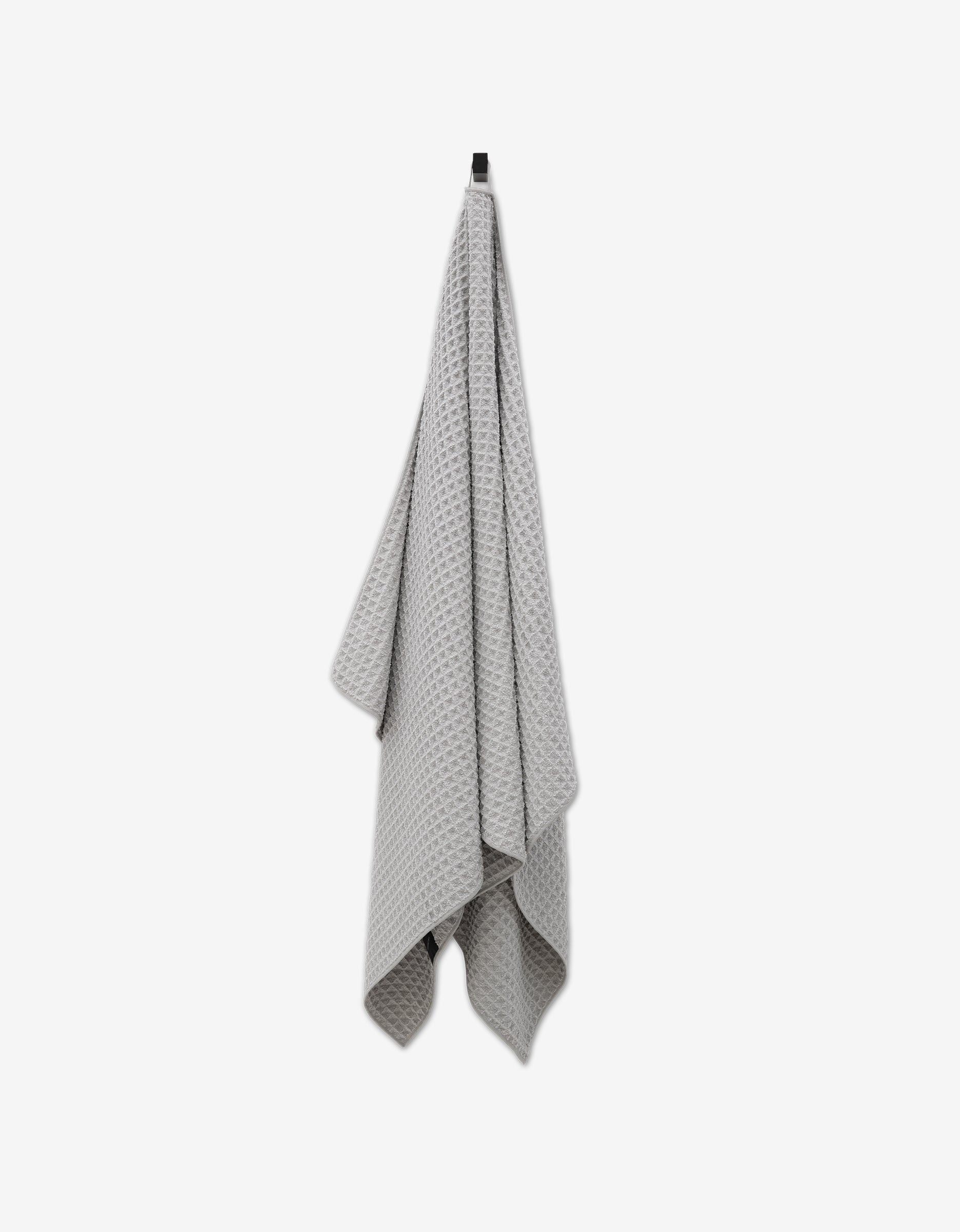 The GEOMETRY Stone Waffle Bath Towel in light gray hangs from a hook against a white background, offering ultra-absorbent luxury and waffle-textured elegance to your bathroom.