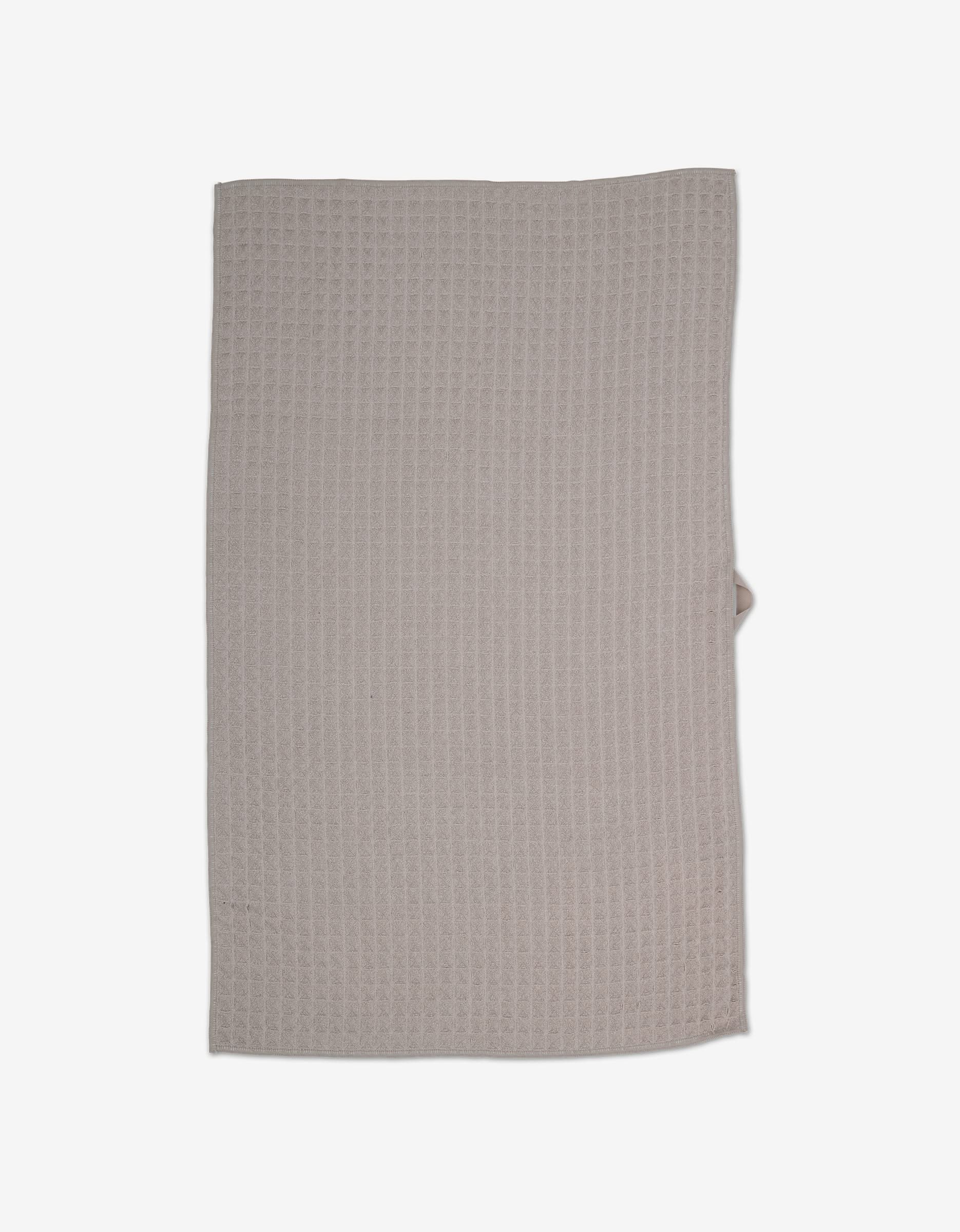 A taupe, rectangular waffle-textured kitchen towel from GEOMETRY, crafted from recycled materials, is laid flat on a white background.