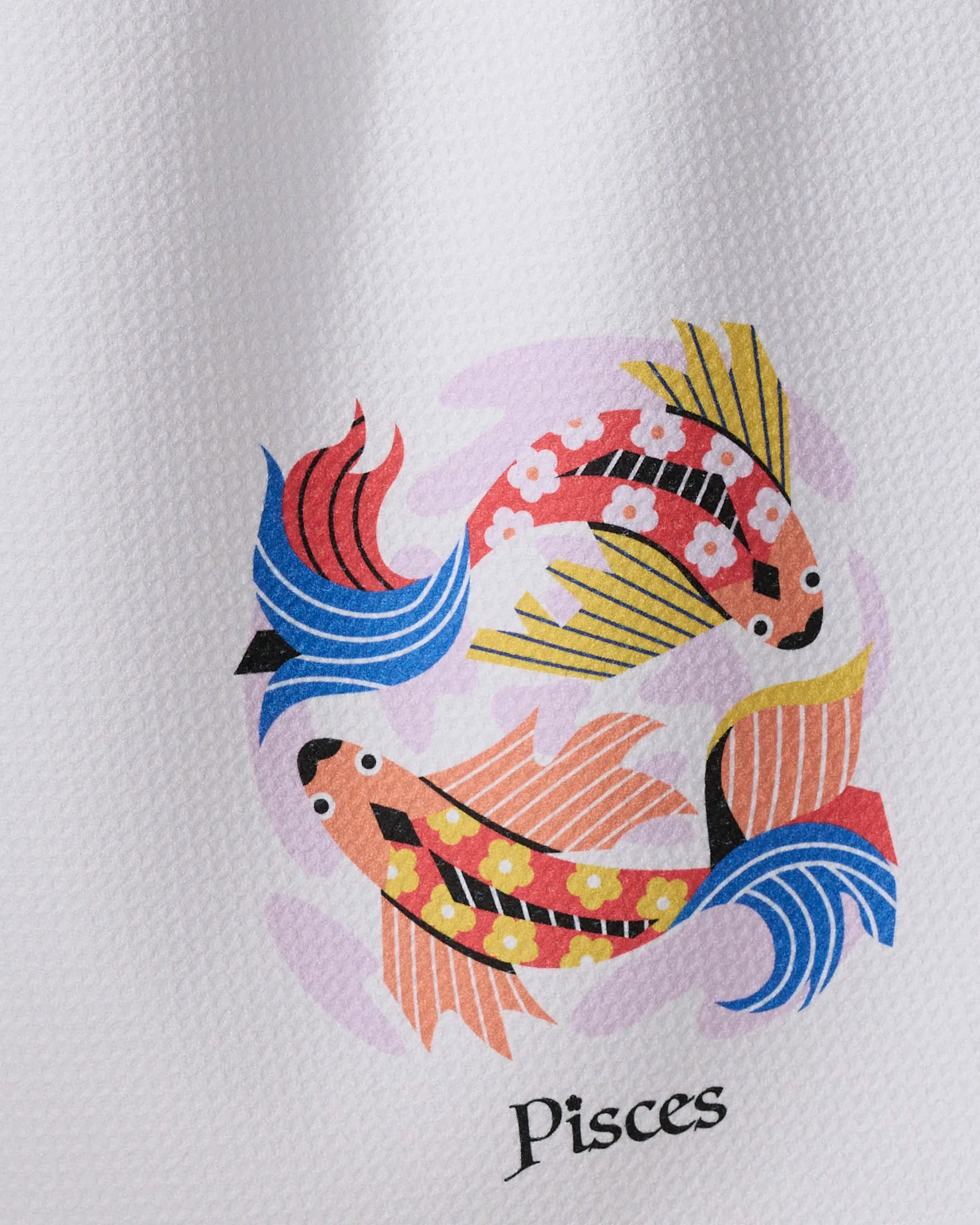 Two colorful, stylized fish with floral and geometric patterns swim in a circle on a white textured background. "Dreamy Pisces" by Heather Zhou is an ultra-absorbent tea towel made from recycled materials, perfect for your kitchen.