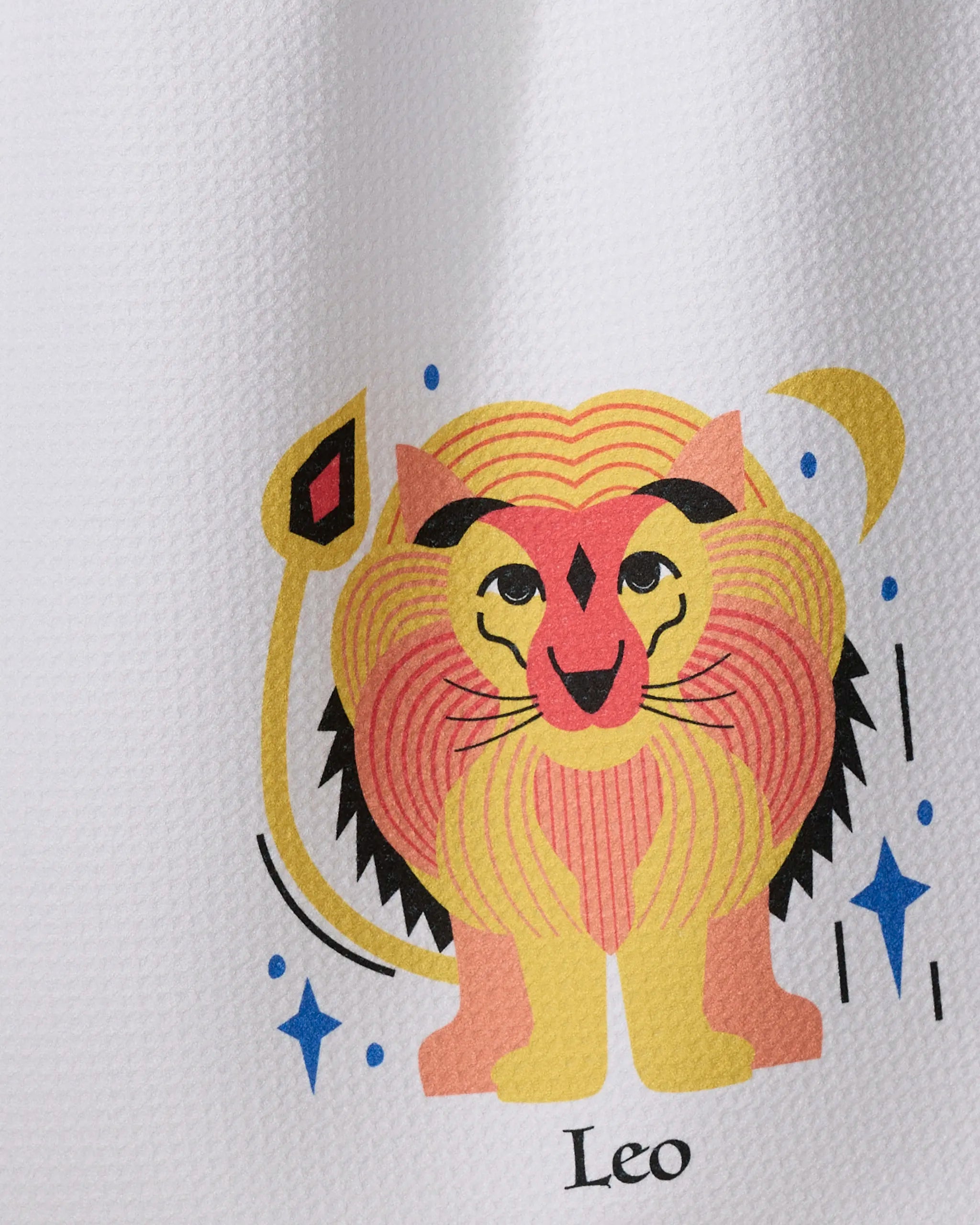 Glowing Leo by Heather Zhou: a quick-drying tea towel made from recycled materials, featuring a stylized lion with a colorful mane, blue eyes, curled tail, blue stars, and "Leo" below on white textured fabric.