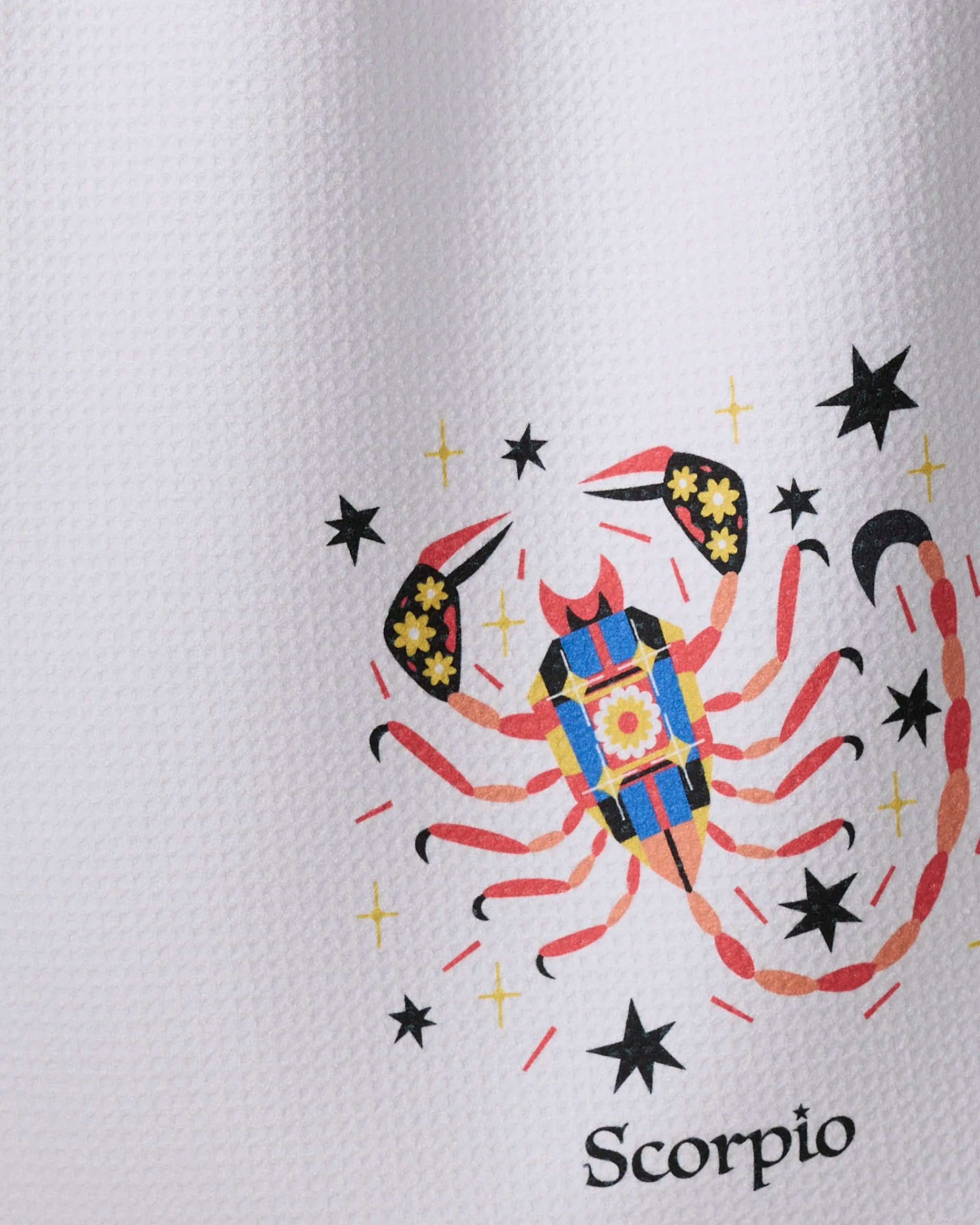 The "Mysterious Scorpio" tea towel by Heather Zhou features a colorful scorpion with black stars and yellow sparkles on a white textured, recycled, ultra-absorbent fabric, with "Scorpio" printed beneath the illustration.