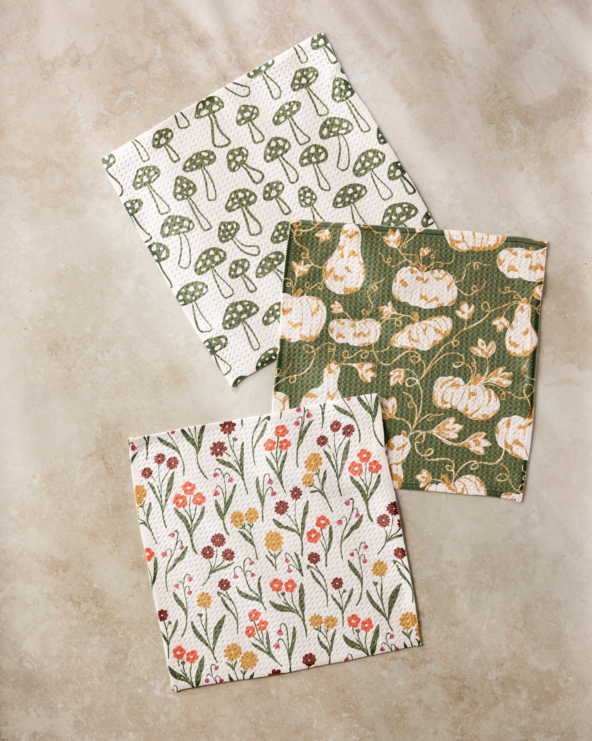 The Kayla Ann Woodland Trail set features three recycled patterned cloths: green mushrooms, orange pumpkins with vines on green, and small colorful flowers and leaves, displayed on a beige surface.