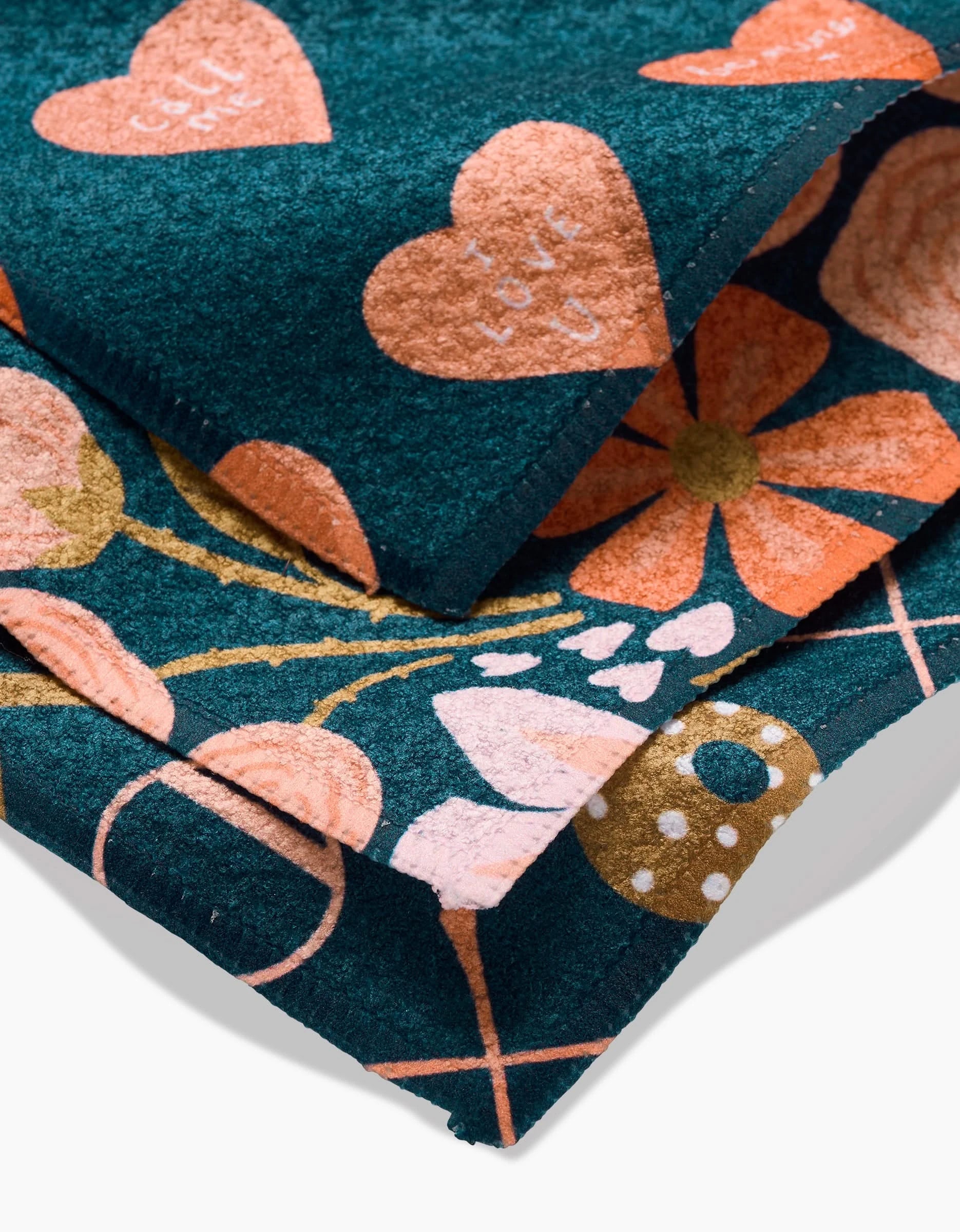 Amy MacCready’s Amandine dishcloths showcase stacked Geoweave fabric with vibrant floral and heart designs in orange, pink, and cream on dark teal—a unique and colorful addition to your kitchen.