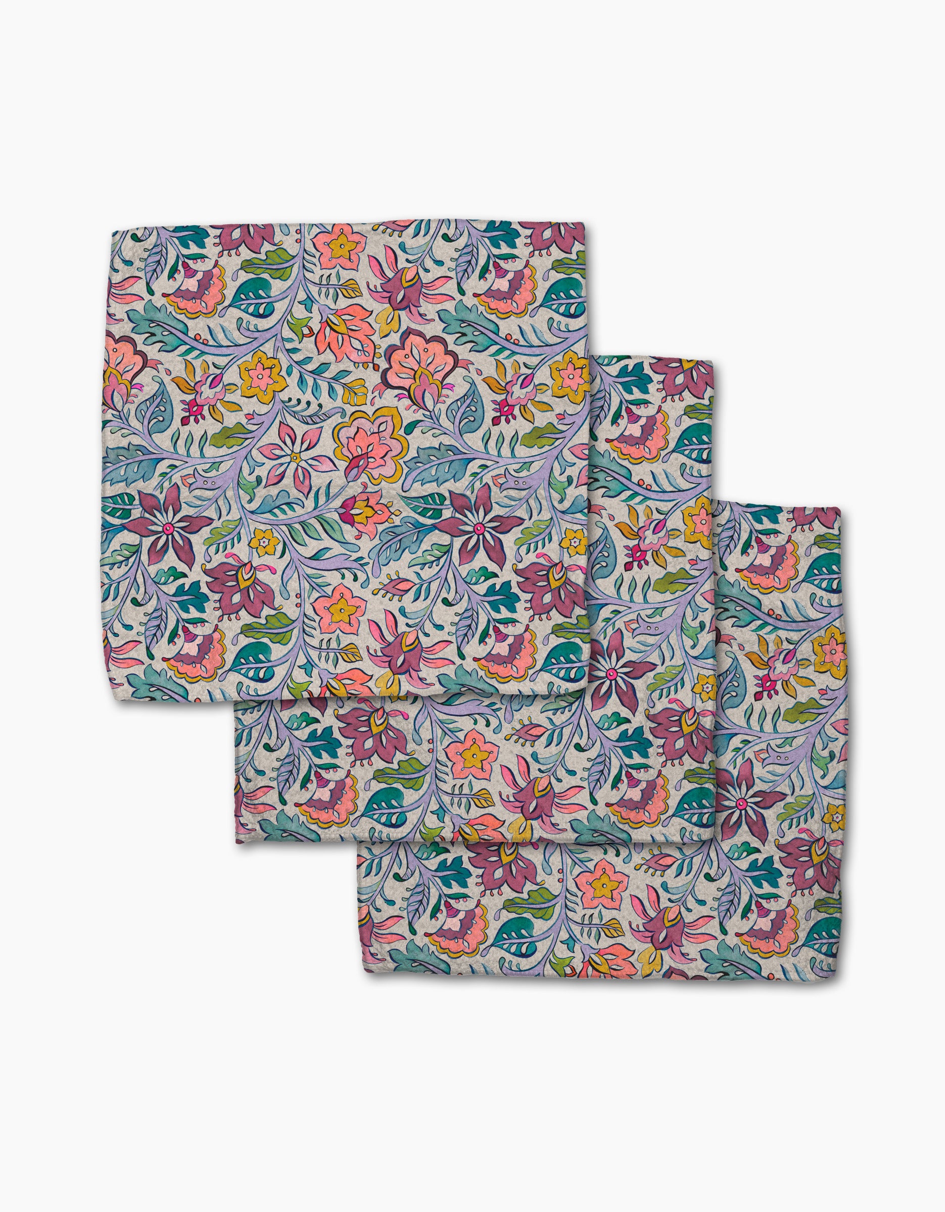 Three "Amethyst" square cloth napkins by Maayan Alper-Swan, made from recycled materials, feature a colorful floral pattern with pink, yellow, and orange flowers plus green leaves and vines on a light background, arranged in a stacked set.