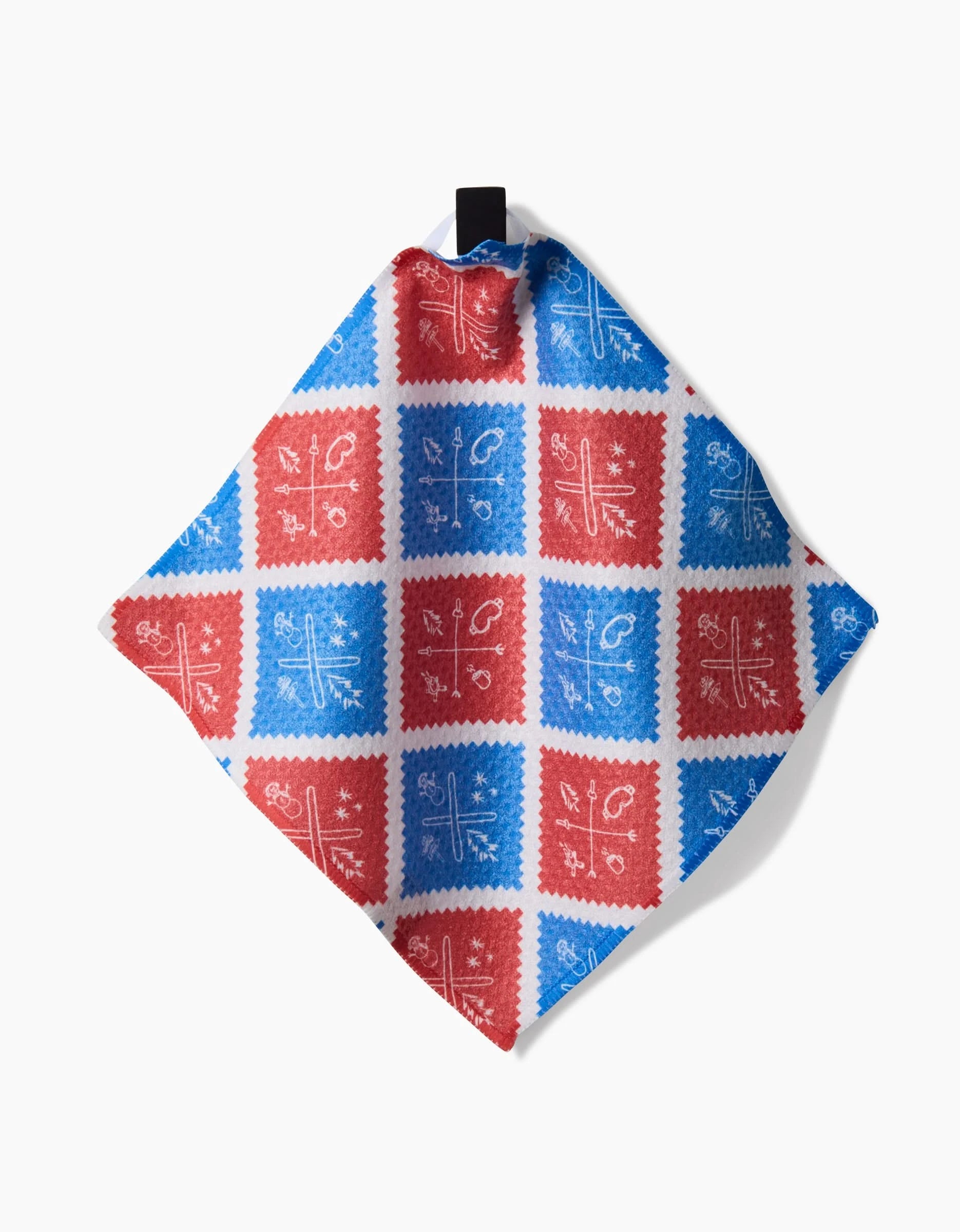 The Rosa Kichline Apres Ski tea towel features red and blue squares with white floral and geometric designs on Geoweave fabric, plus a black corner loop for convenience. The napkin is shown flat on a white background.