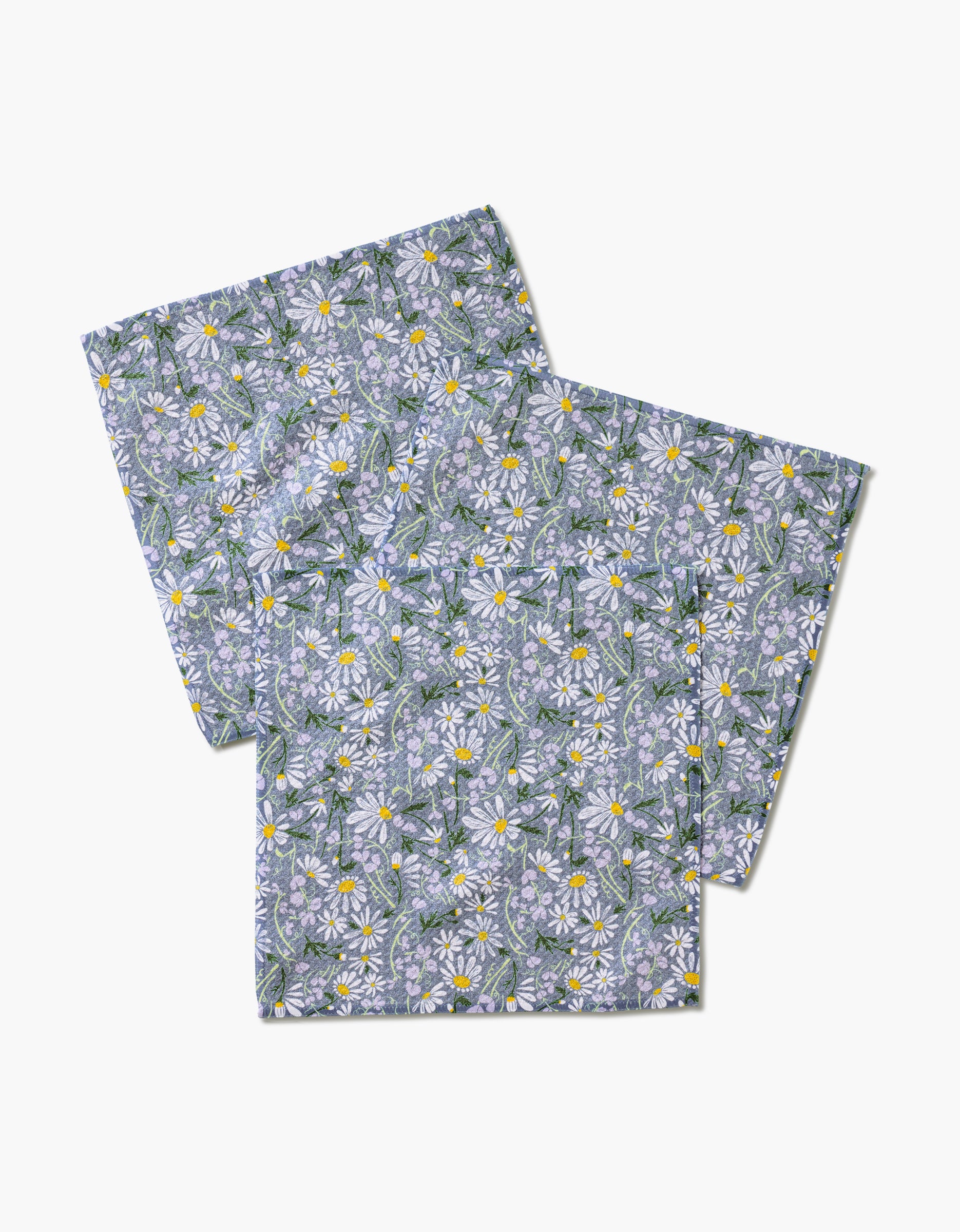 Two folded April pillowcases by Elisabeth Wing, featuring white daisies with yellow centers and green leaves on a light blue background, made from eco-friendly fabric, displayed on a plain white surface.