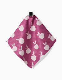 The “Autumn Party” reusable dishcloth by Claire Iglesias, in pink with a white apple and leaf pattern, hangs by a black loop against a white background.