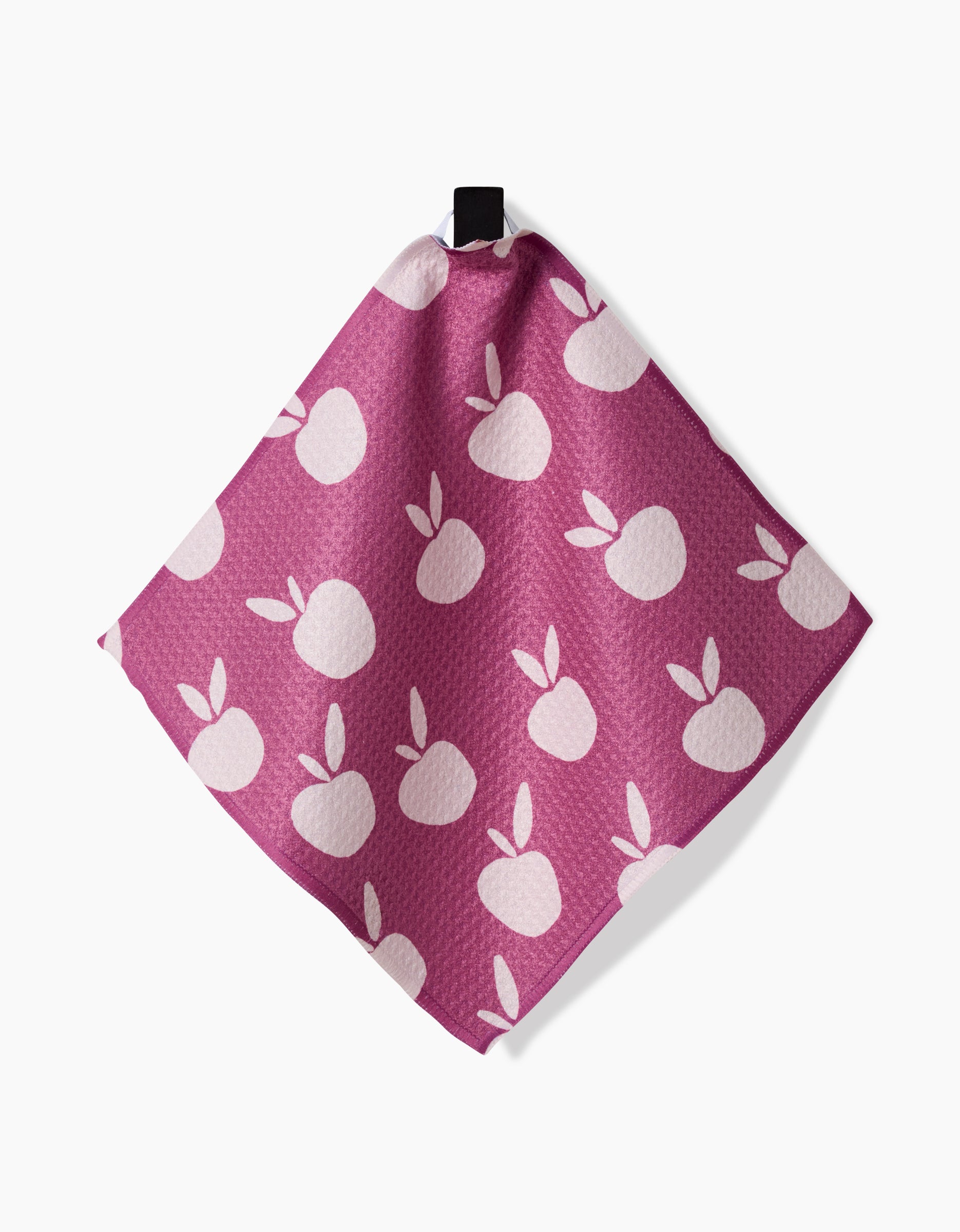 The “Autumn Party” reusable dishcloth by Claire Iglesias, in pink with a white apple and leaf pattern, hangs by a black loop against a white background.