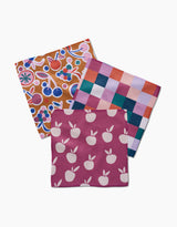Claire Iglesias’ Autumn Party set features three colorful, reusable dishcloths: magenta with white apples, a vibrant red-blue-pink-purple checkered towel, and one with a multicolored fruit-floral design—an eco-friendly kitchen essential.