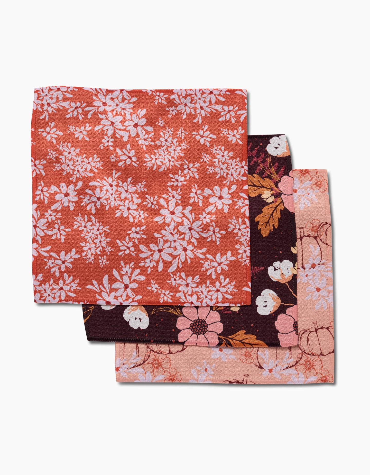 Three stacked Autumnal Reverie napkins by Ashley Celena—crafted from recycled materials—feature unique floral designs in red, maroon, and pink on a white background.