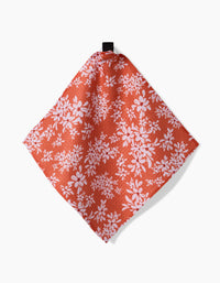 Ashley Celena’s “Autumnal Reverie” is a red cloth napkin with a white floral pattern, made from recycled materials, shown hanging by a black loop against a plain white background.