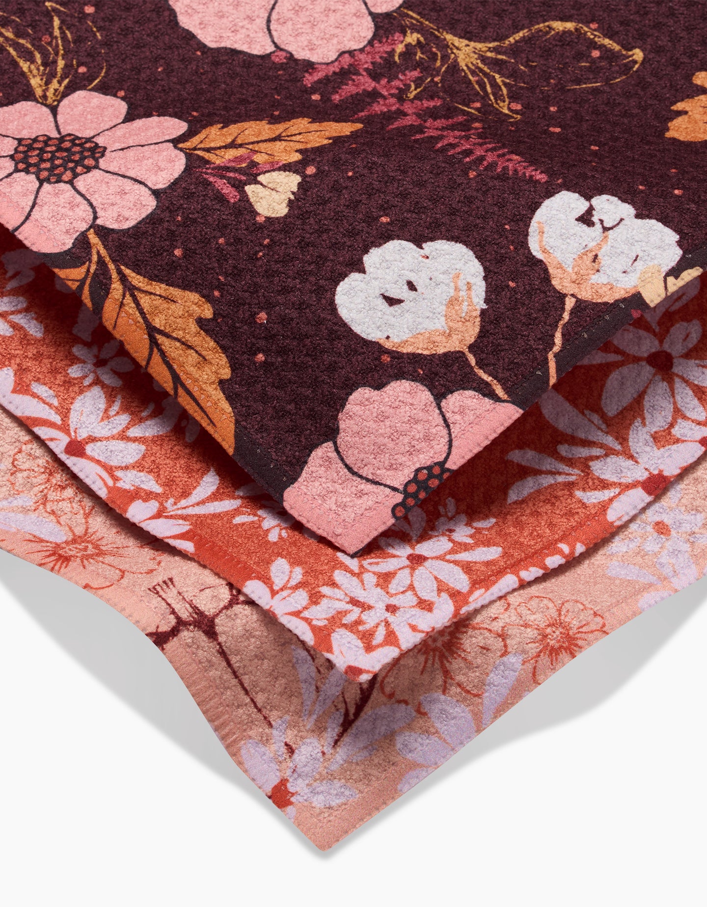 The Autumnal Reverie dishcloth set by Ashley Celena includes three recycled-fabric layers: a dark floral top, a rusty red middle with pink blooms, and a light pink bottom—each featuring unique floral patterns.