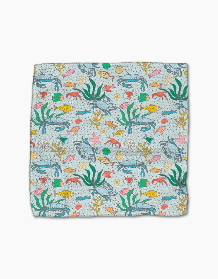 The Mindfulnice Beneath the Waves dishcloth set features a vibrant underwater pattern of fish, seaweed, starfish, shells, and coral on light blue. Made from recycled materials for an eco-friendly clean.