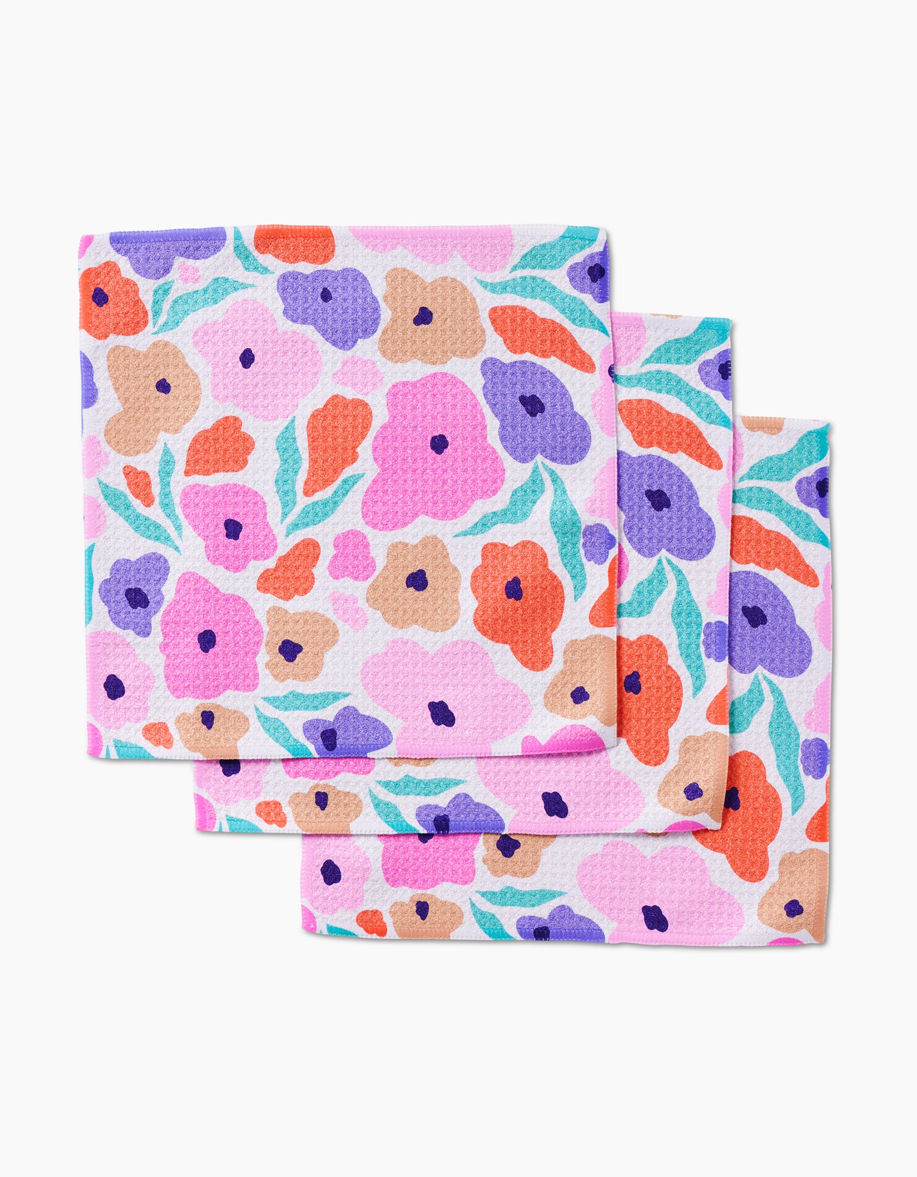 The GEOMETRY Blossoming Love set includes three folded reusable dishcloths, made from recycled materials and featuring a vibrant floral pattern in orange, purple, pink, red, and green on a light background.