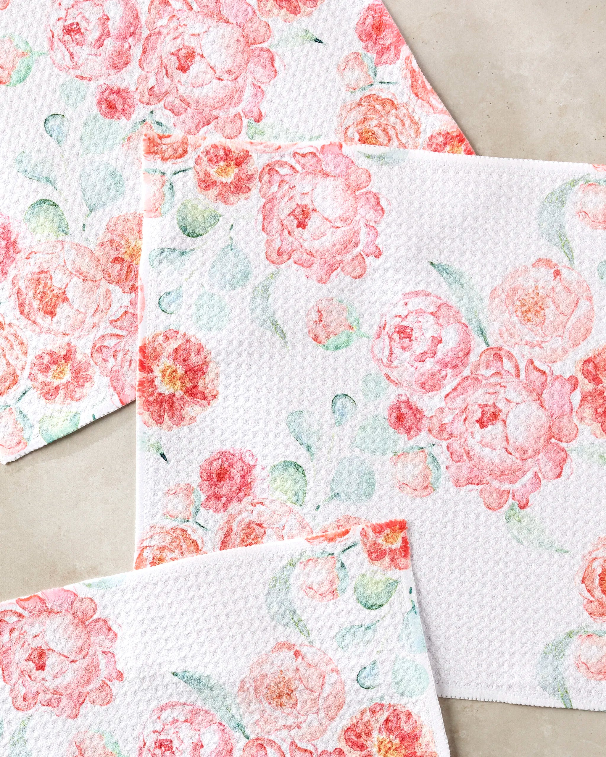 Blush Florals by Elena Fay: white, textured, super-absorbent dishtowels featuring pink and red watercolor-style flowers with green leaves, displayed on a beige surface.