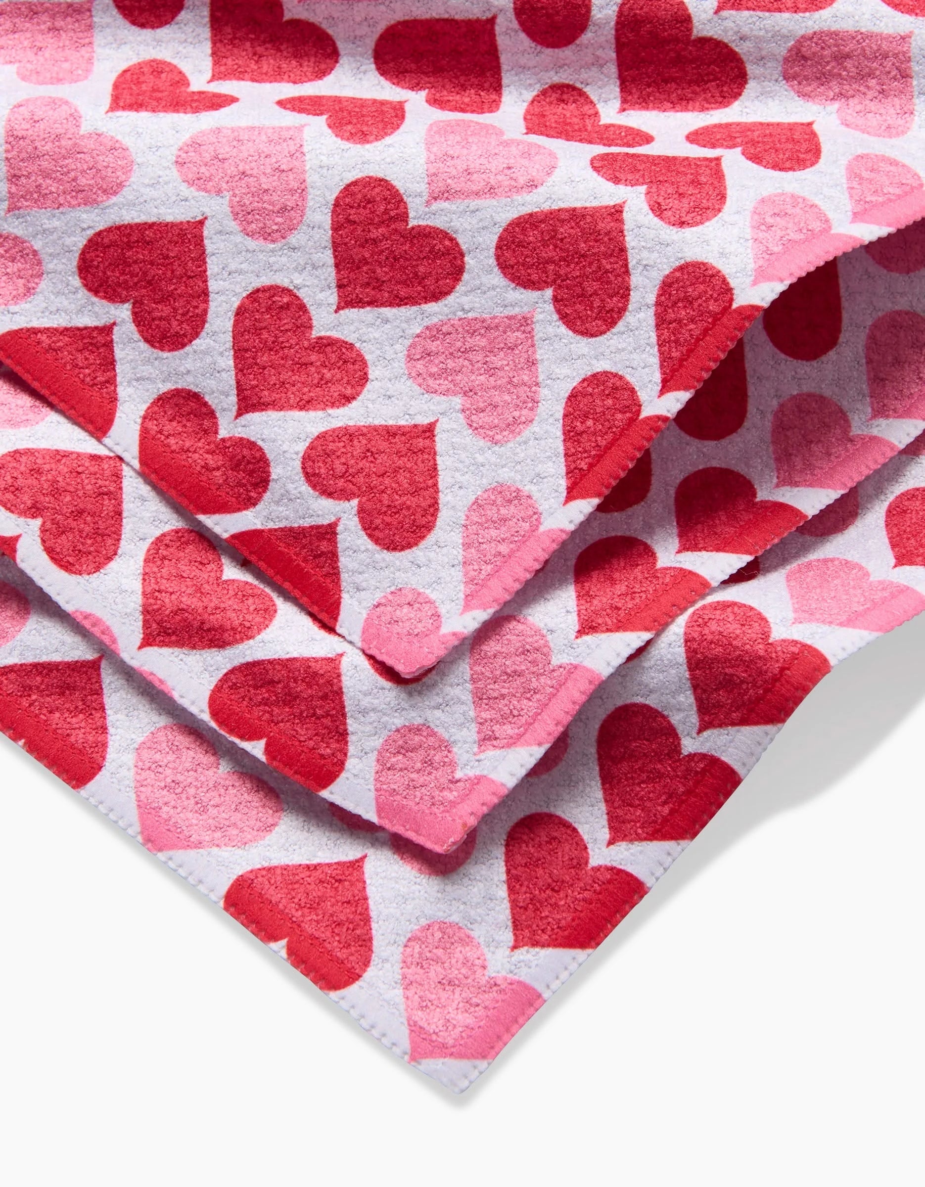 A close-up of Blushing Hearts by Danelys Sidron shows soft, cozy dishcloths with pink and red heart patterns on white and stitched edges—perfect for bringing charm to your kitchen.