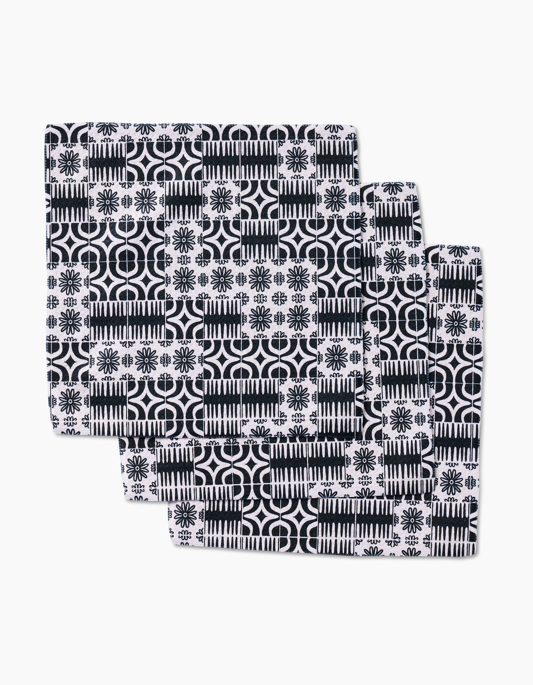 Three Bohemian Mosaic dishcloths by GEOMETRY are stacked, each made from Geoweave fabric and featuring black and white geometric and floral tile-inspired designs.