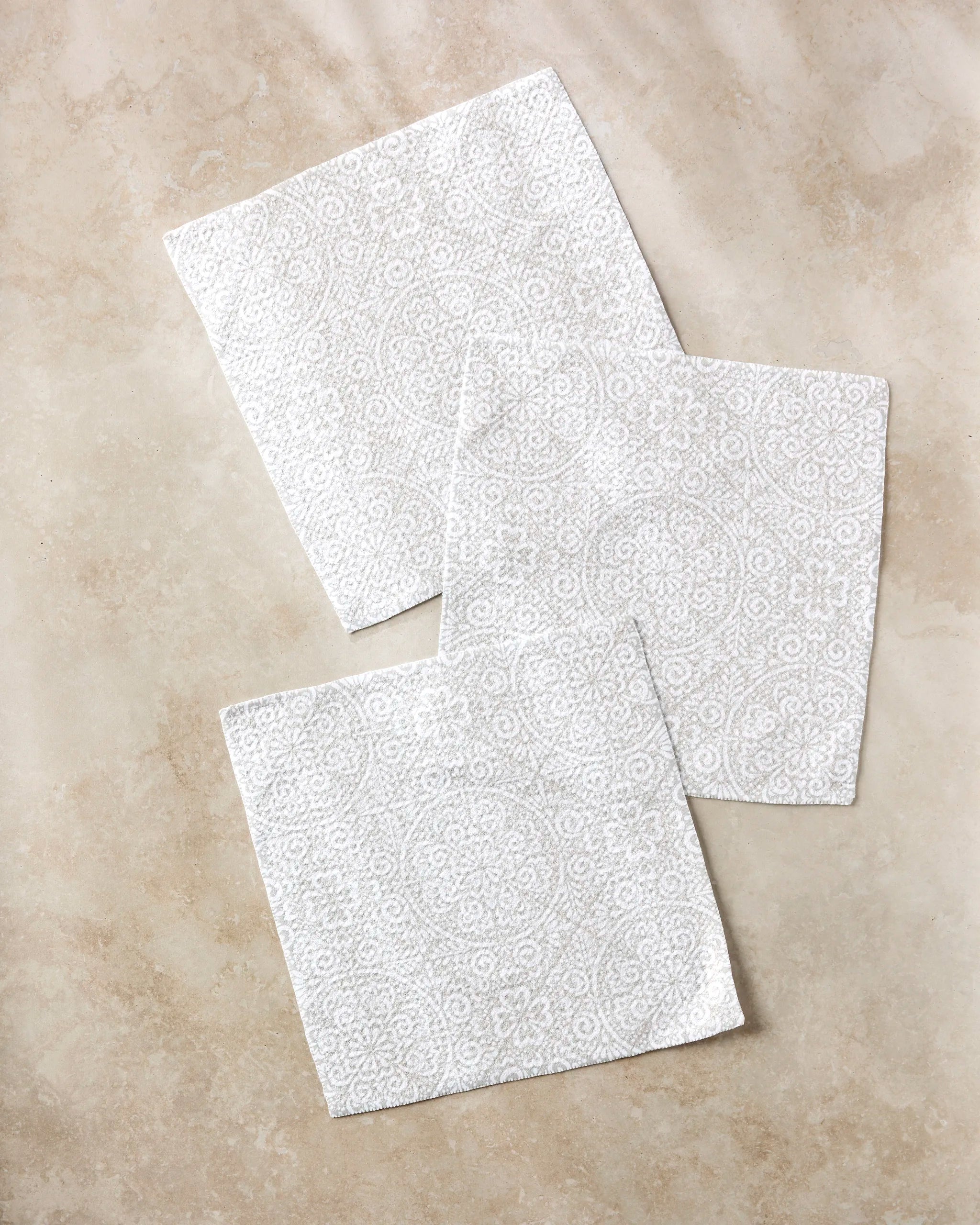 Three Boho Medallion napkins by Kris Ruff, featuring a subtle circular and floral pattern, are displayed on beige marble—a stylish, eco-friendly choice perfect for those who love recycled material dishcloth sets.