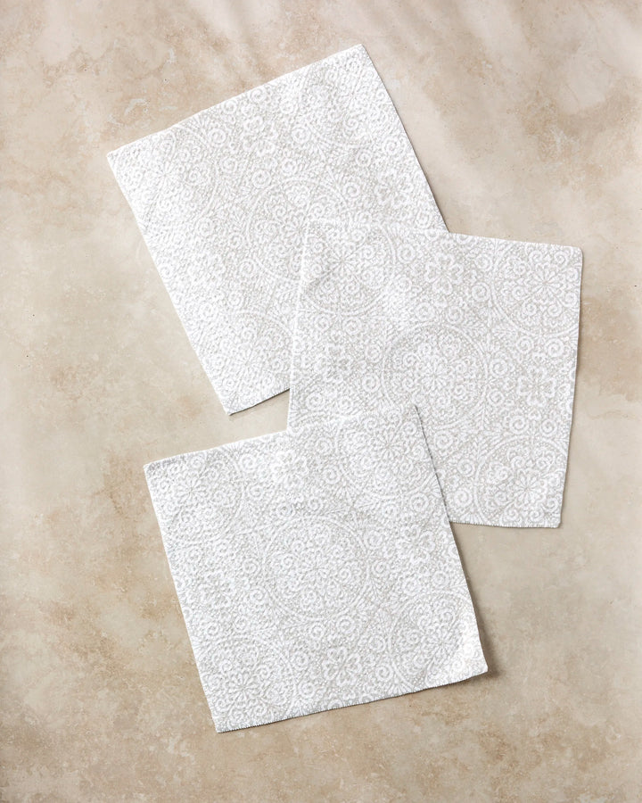 Three Boho Medallion napkins by Kris Ruff, featuring a subtle circular and floral pattern, are displayed on beige marble—a stylish, eco-friendly choice perfect for those who love recycled material dishcloth sets.