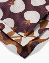 A close-up of Bold Fall dishcloths by Lizzie Clark, folded to show their textured, recycled fabric with large white and brown abstract shapes on a dark maroon background.