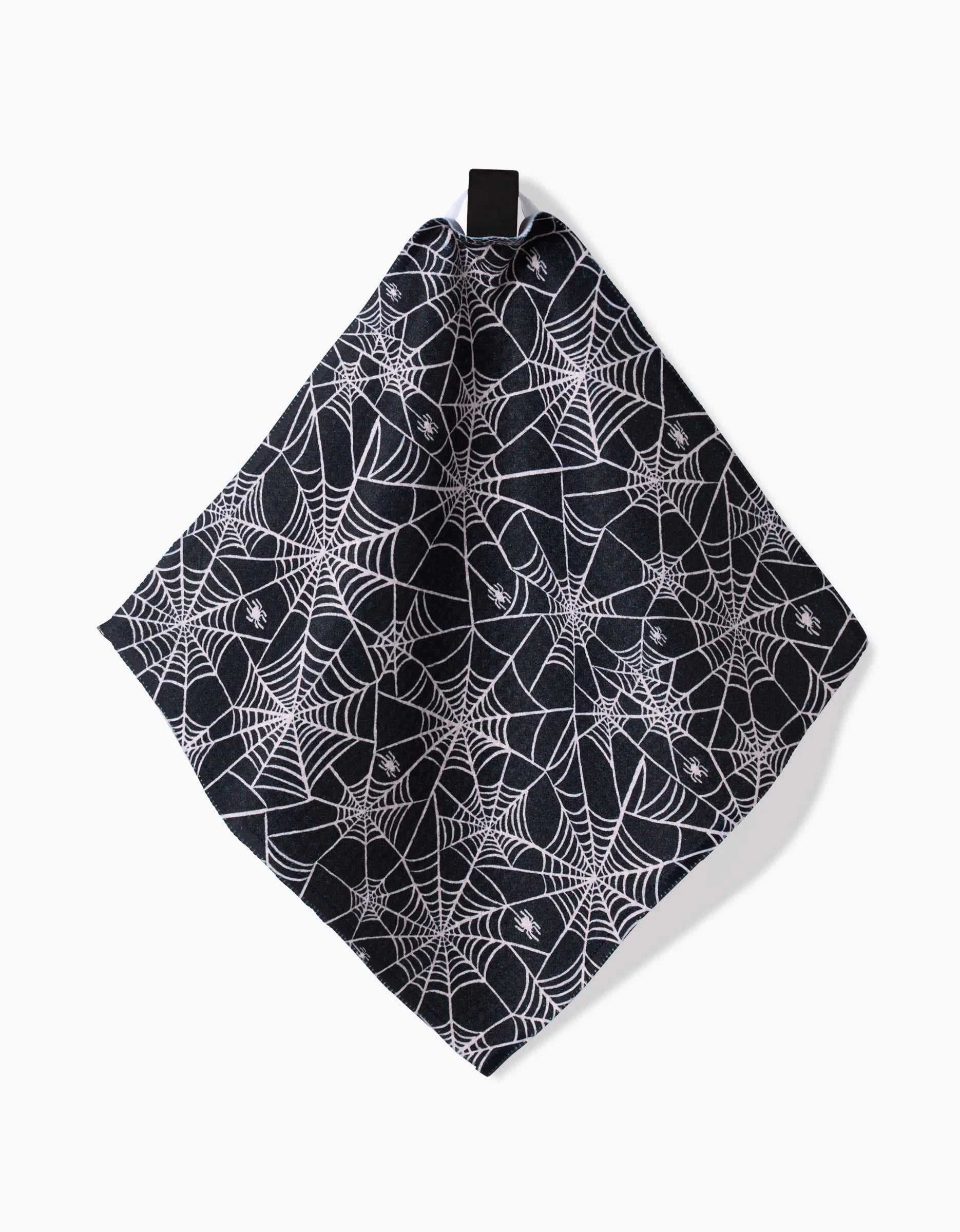 The Booos napkin by Kayla Ann is made from black Geoweave fabric with a white spiderweb pattern, and hangs at an angle from a black loop against a white background.