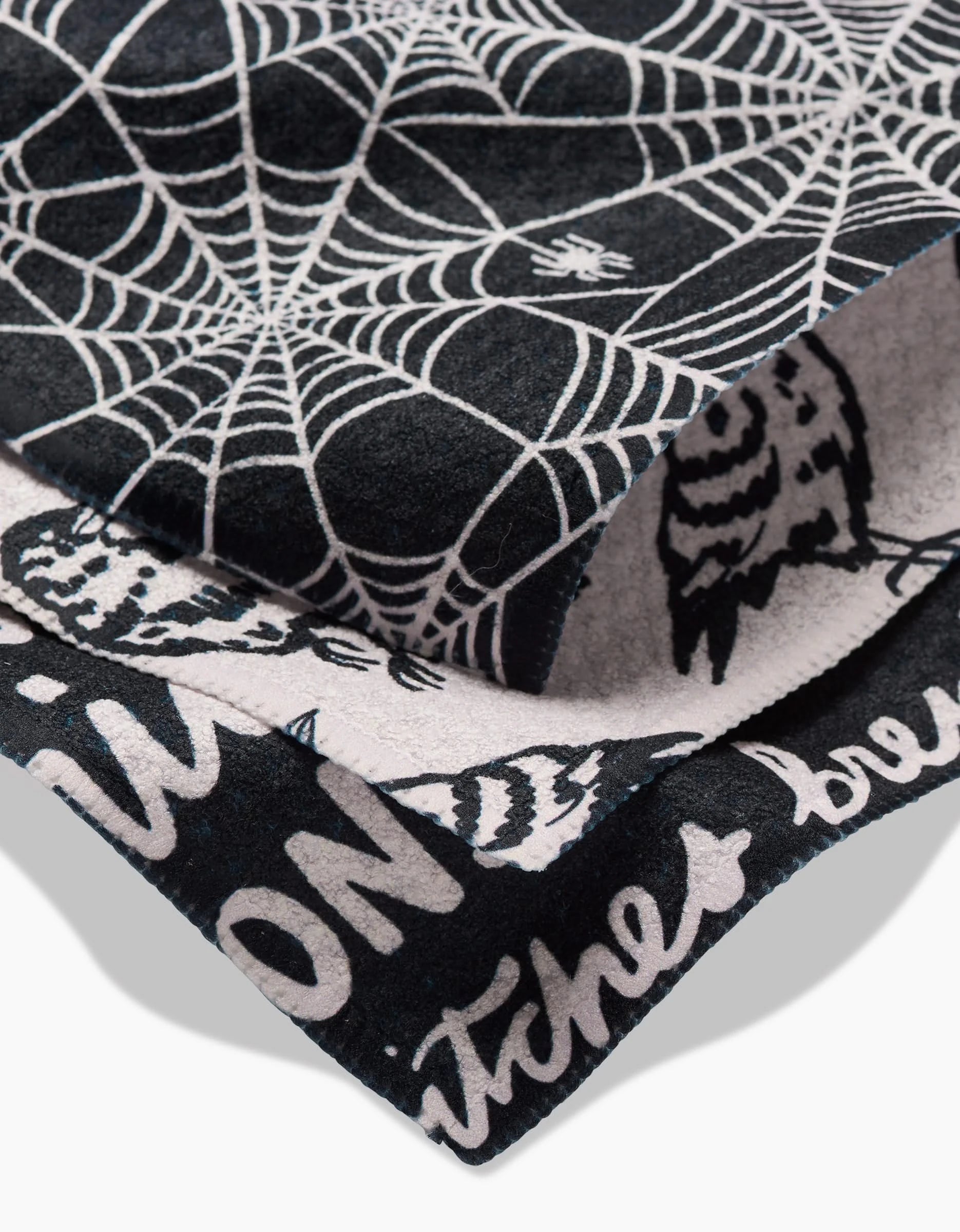 A close-up of Kayla Anns Booos Geoweave dishcloth, showcasing white spiderwebs, owl illustrations, and partial text on a black background.