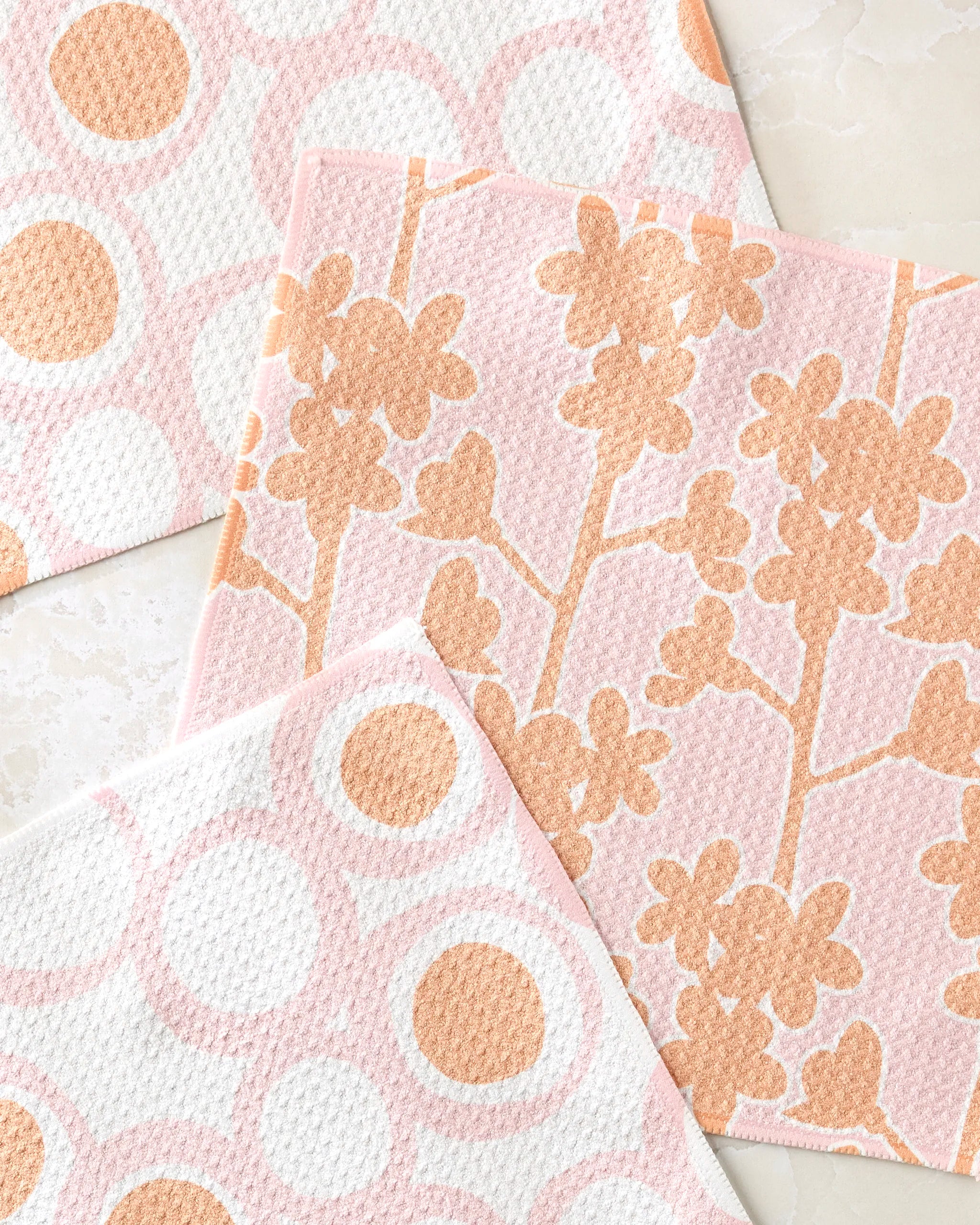 Three Lizzie Clark Bouncing Balls are on a light surface—two with peach and white polka dots, and one with a peach floral branch pattern on pale pink.