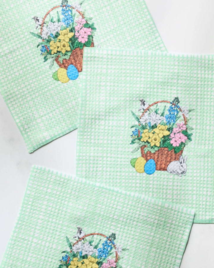 The Geometry Bunny Basket set includes four green textured dishcloths made from recycled materials, each featuring an Easter basket with flowers, colored eggs, and a white rabbit on a white background.