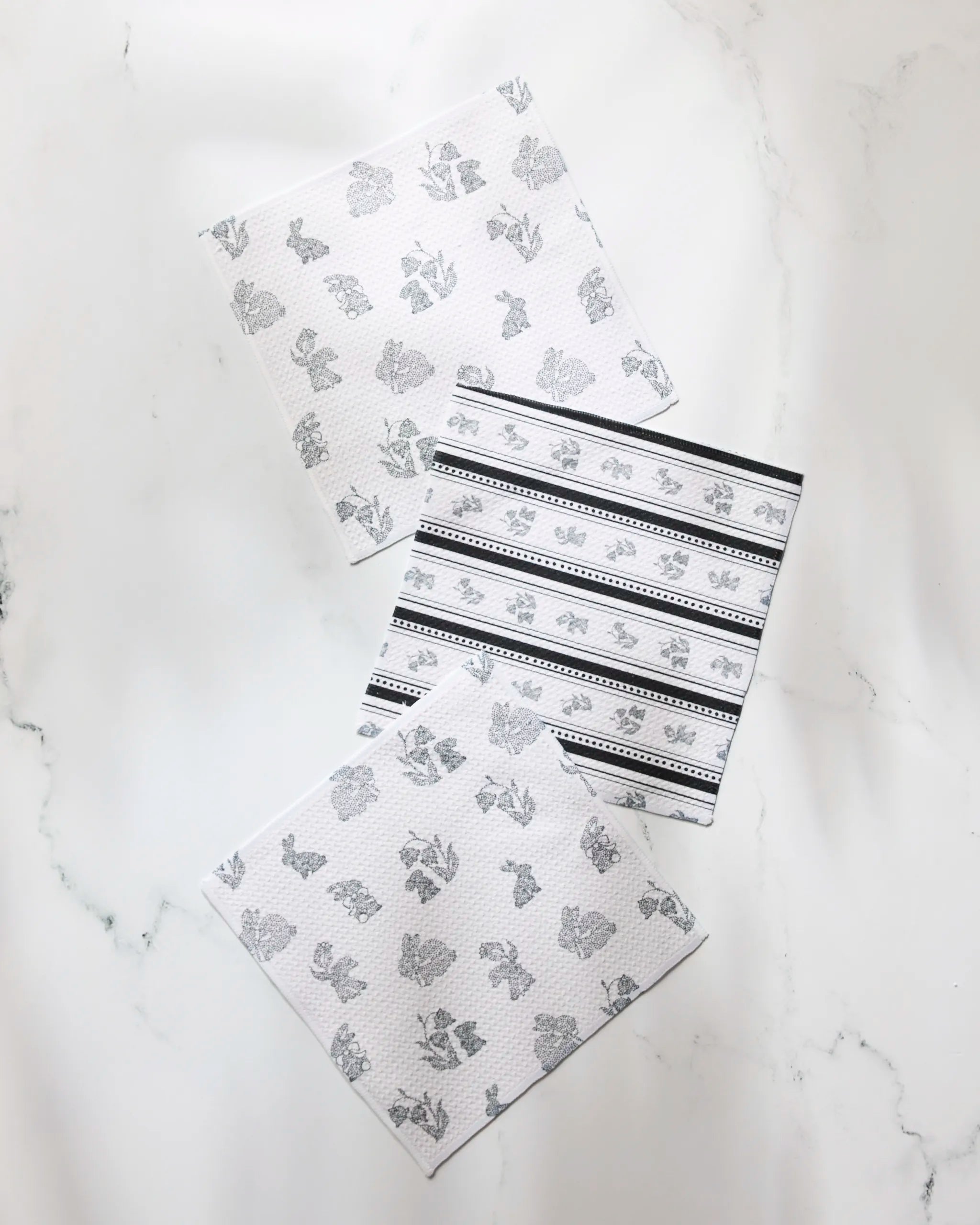 The Geometry Bunny Dots dishcloth set includes three white cloths with light gray patterns and one with black stripes, all crafted from recycled materials for super absorbency and added style in your sustainable kitchen.