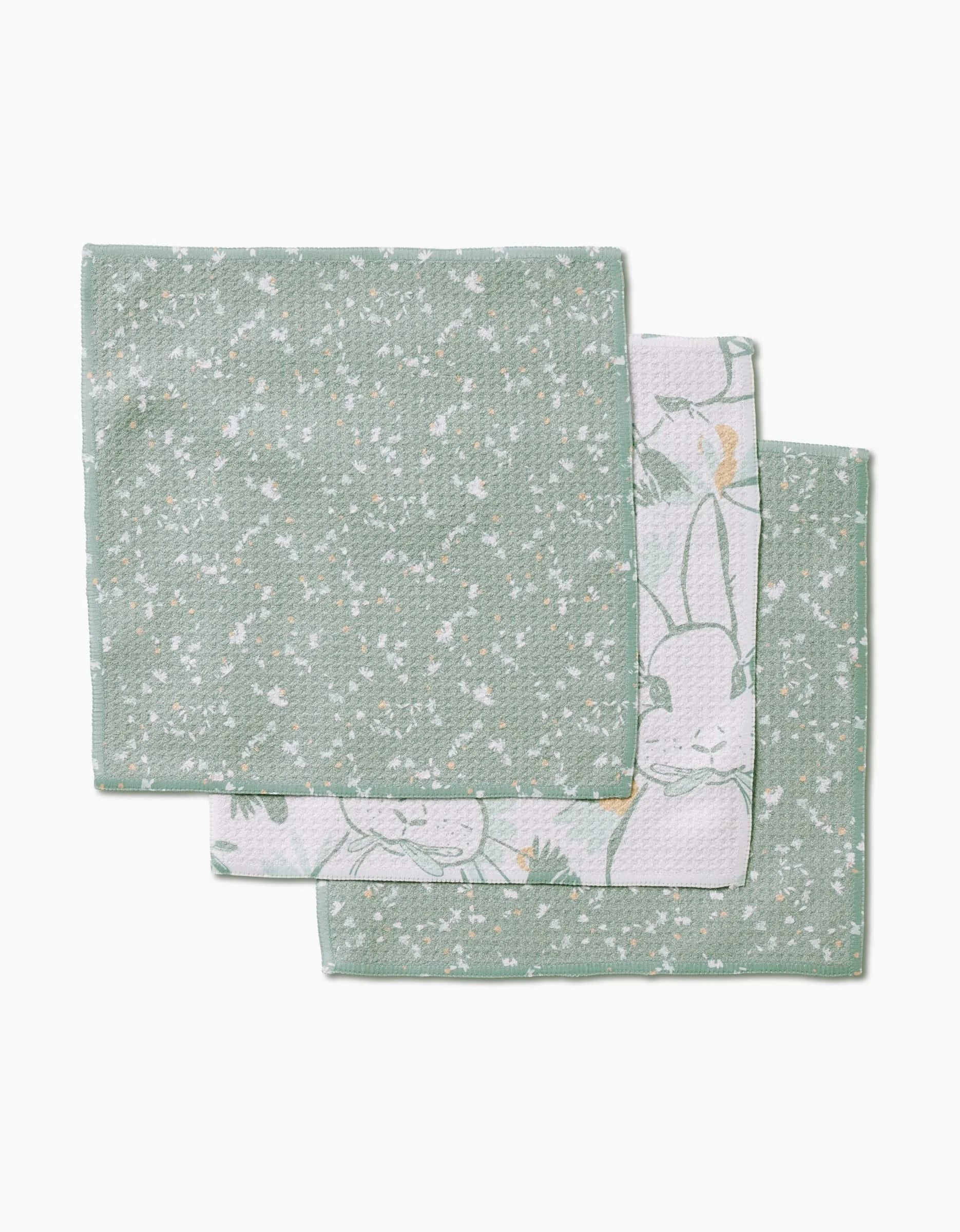 Three folded Bunny Tea Time napkins by Second Nature Studio are stacked: the top shows a green and white speckled design, while the others feature subtle animal and plant outlines in pastel colors on Geoweave fabric.